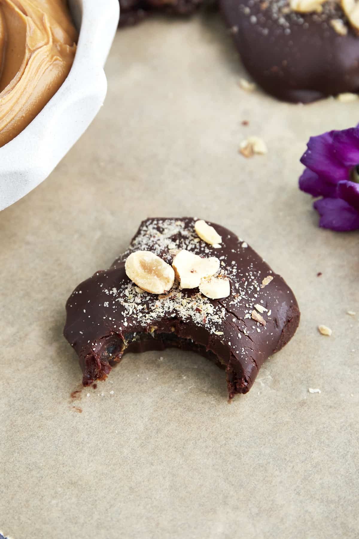 A chocolate covered date topped with peanuts with a bite missing.