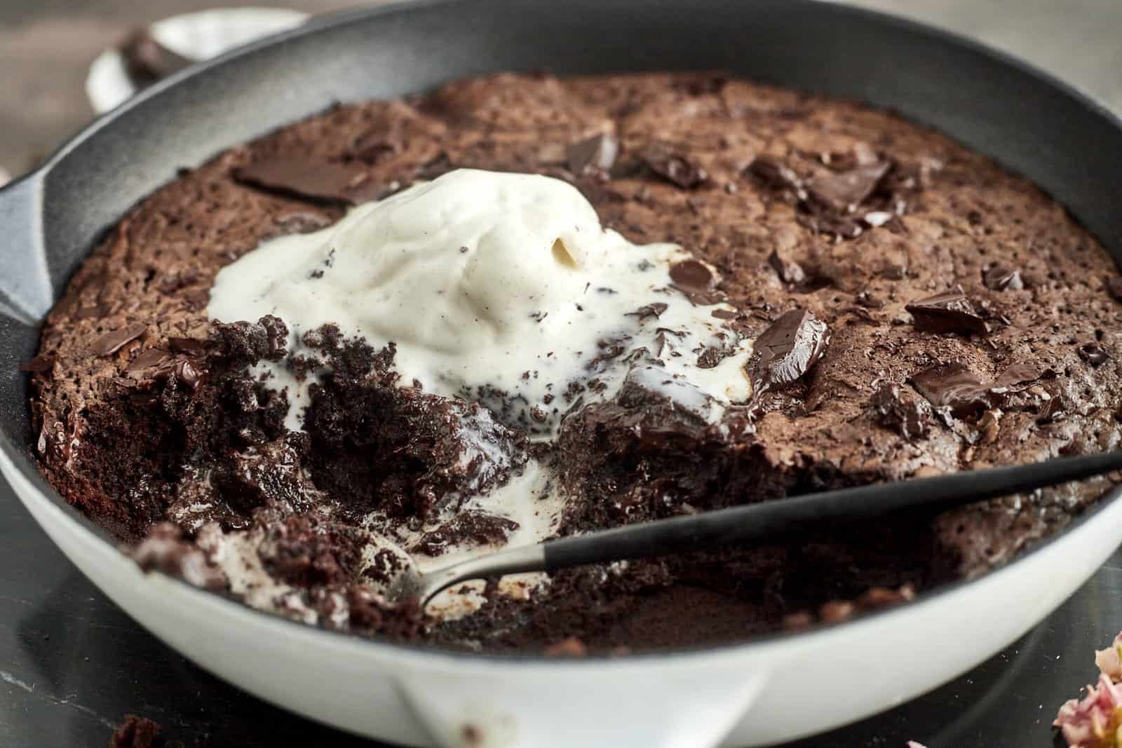 side image of a half-eaten brownie in a skillet topped with melting ice cream