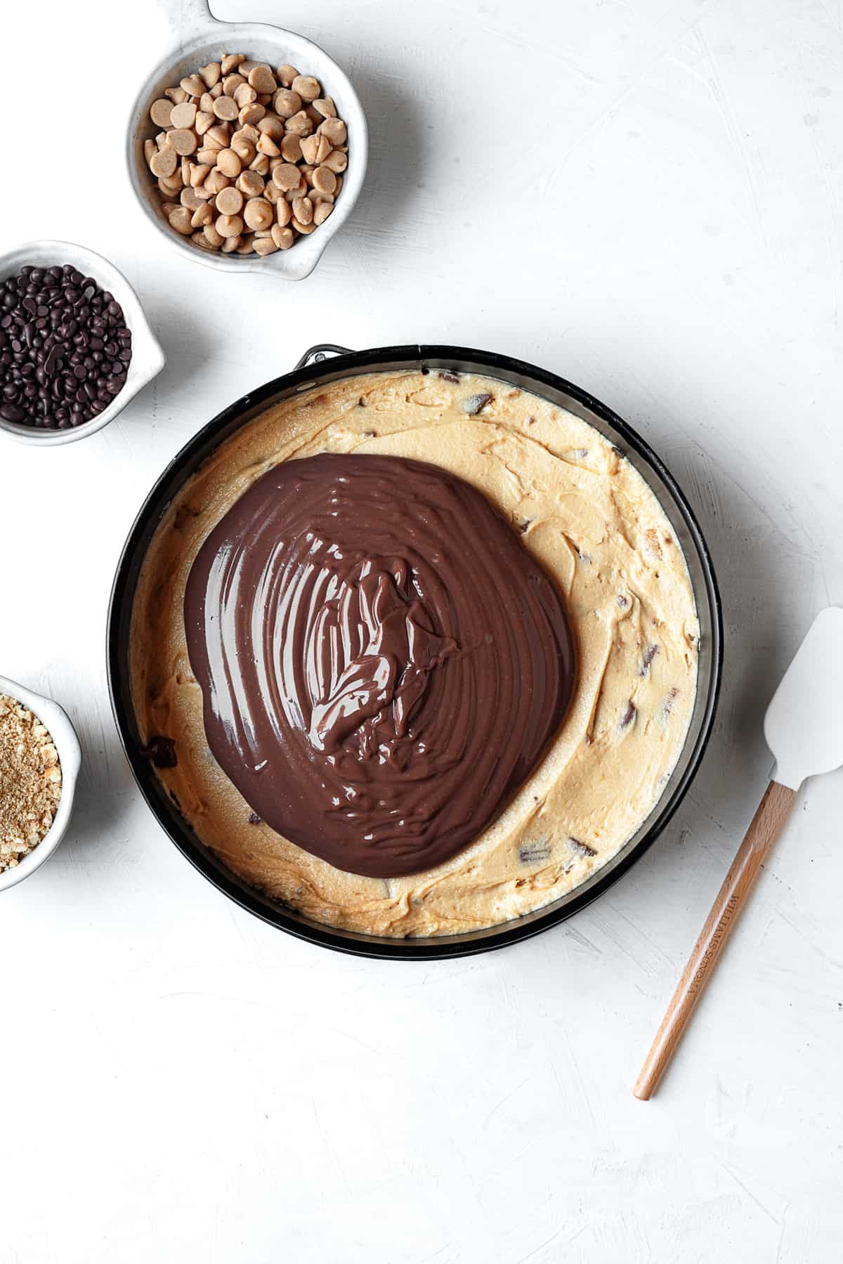 chocolate pudding being spread on top of a layer of peanut butter filing for chocolate peanut butter pie.