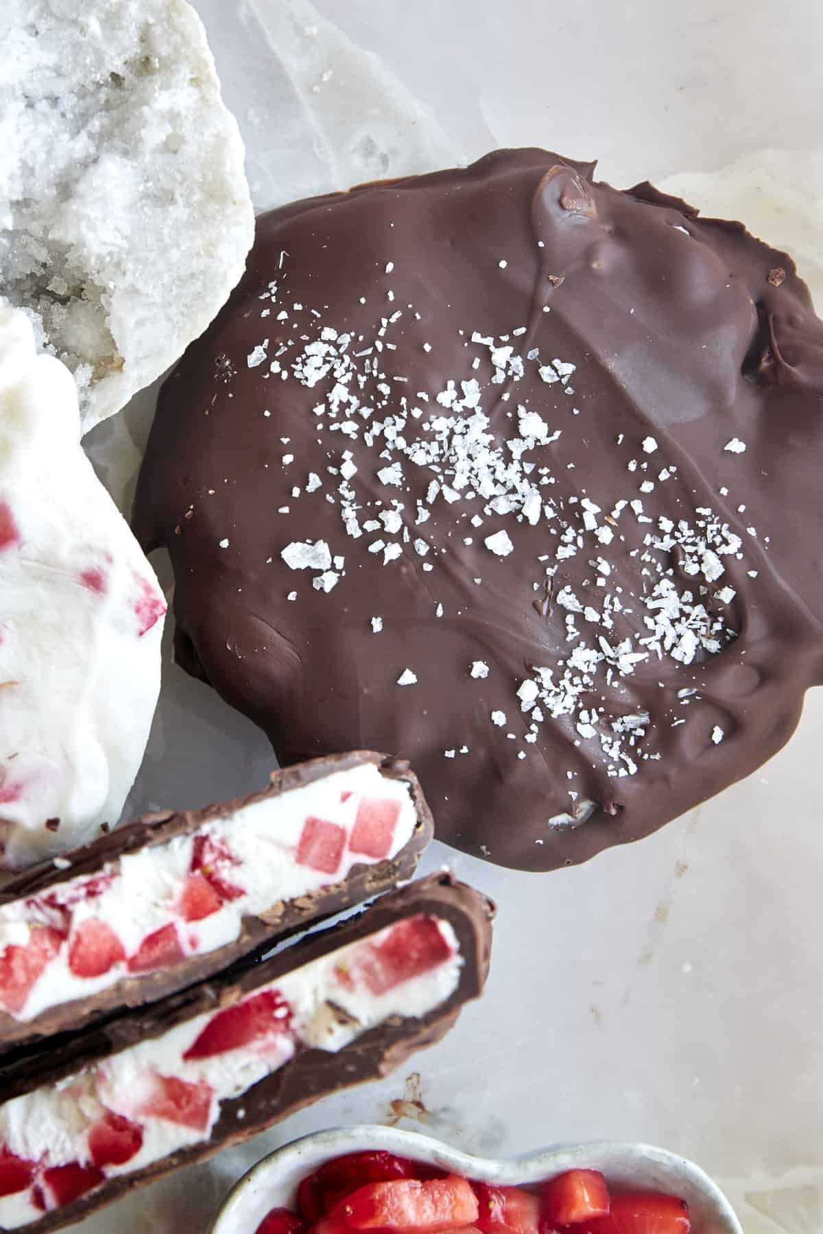 Two chocolate strawberry yogurt clusters topped with salt with one split in half.