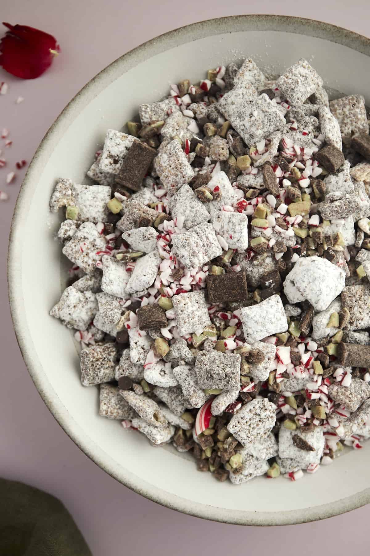 a bowl of Christmas puppy chow with dark chocolate chunks, Andes mints, and peppermint pieces.
