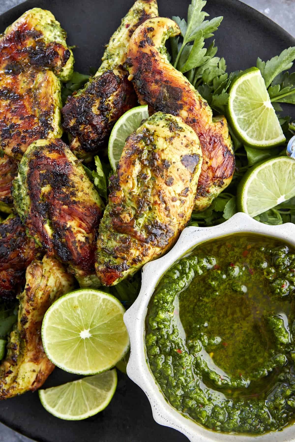Cilantro lime chicken on a plate with zhoug sauce, cilantro, and limes.