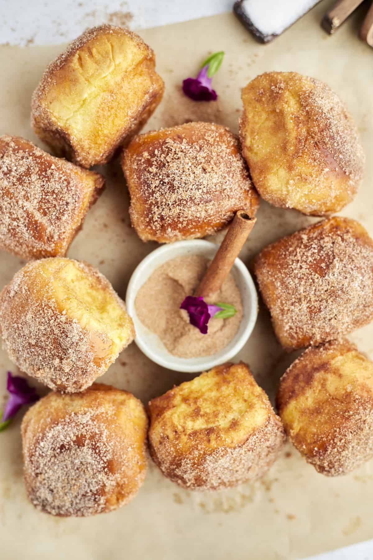 cinnamon french toast buns arranged on parchment paper with a bowl of cinnamon sugar