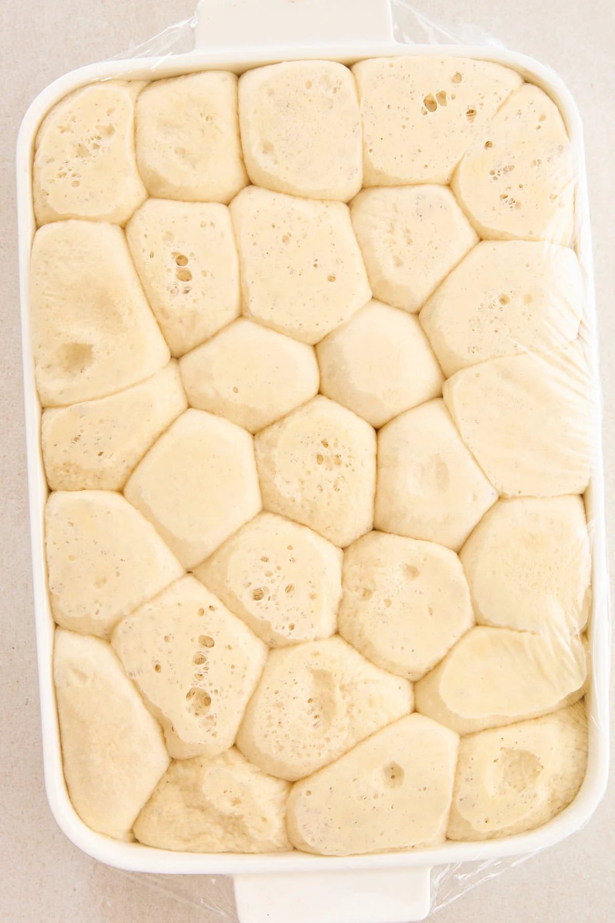 Raw dinner rolls rising in a baking dish.
