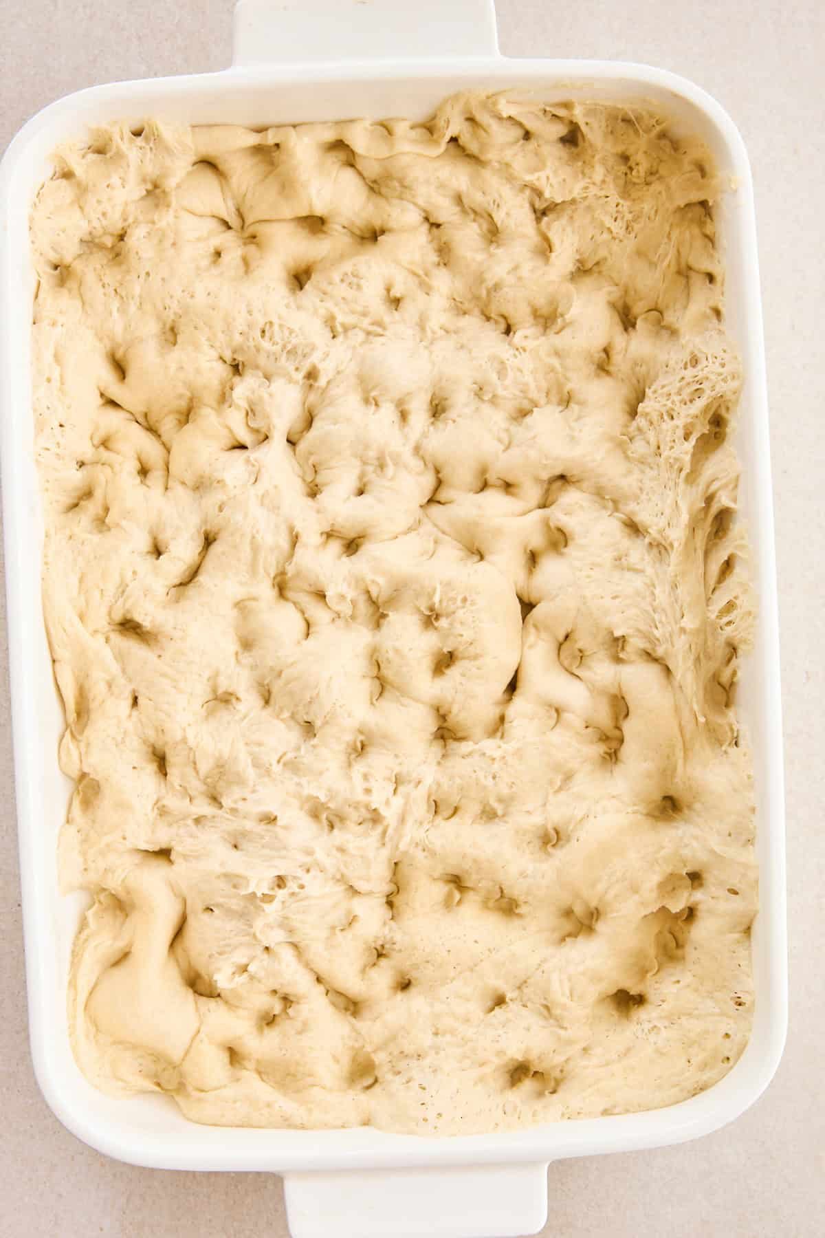 Raw dough pressed down into a baking dish for baked focaccia.