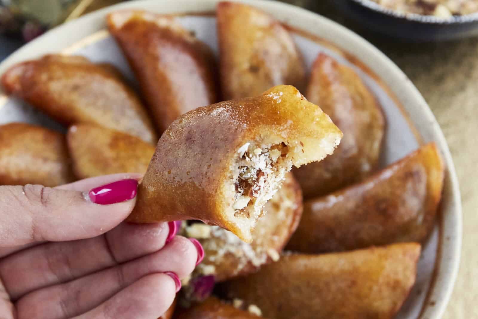a hand holding atayef with a bite taken out of it revealing the chopped nut mixture in the center