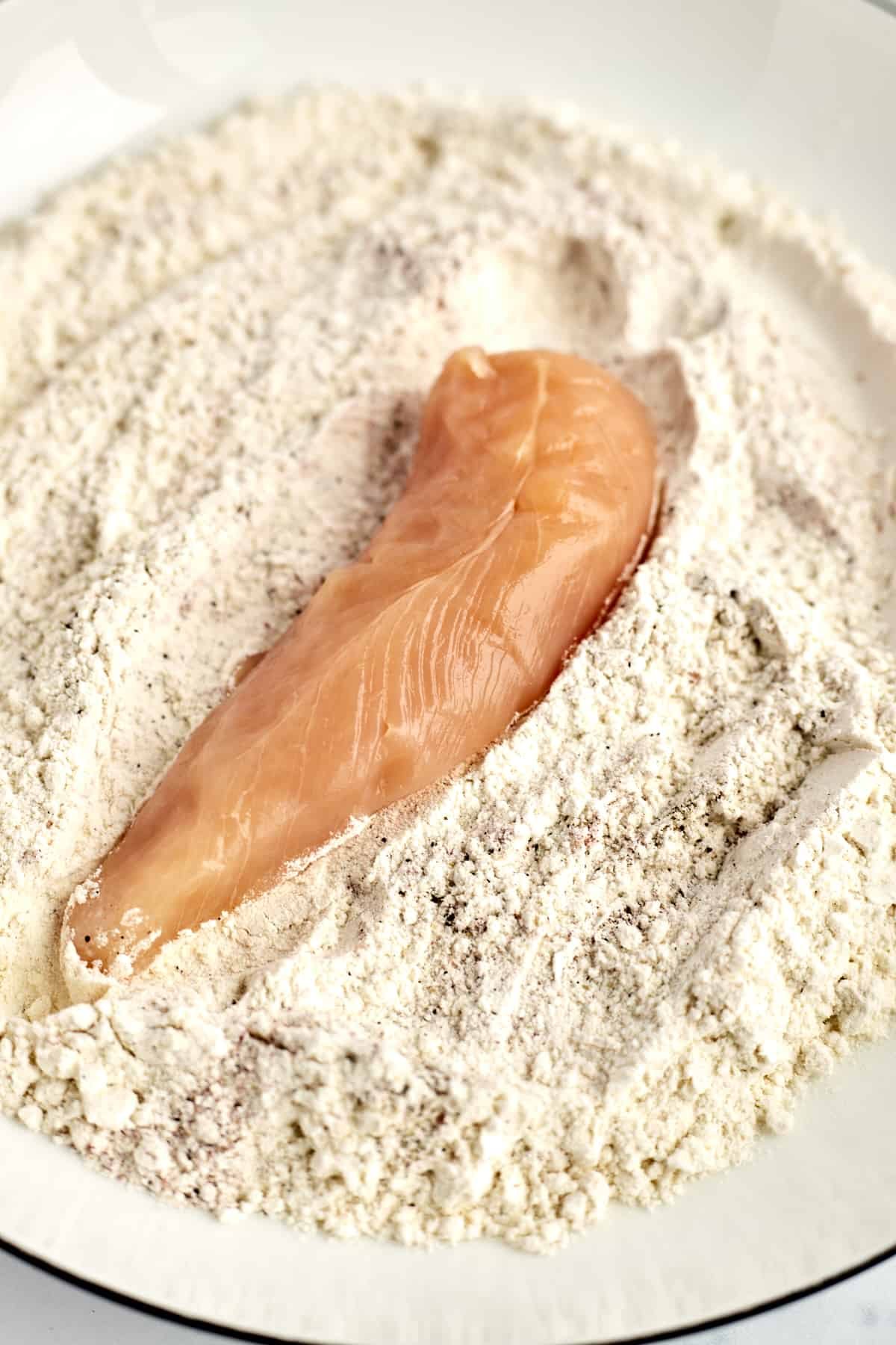 a raw chicken tender in a coconut breadcrumb mixture