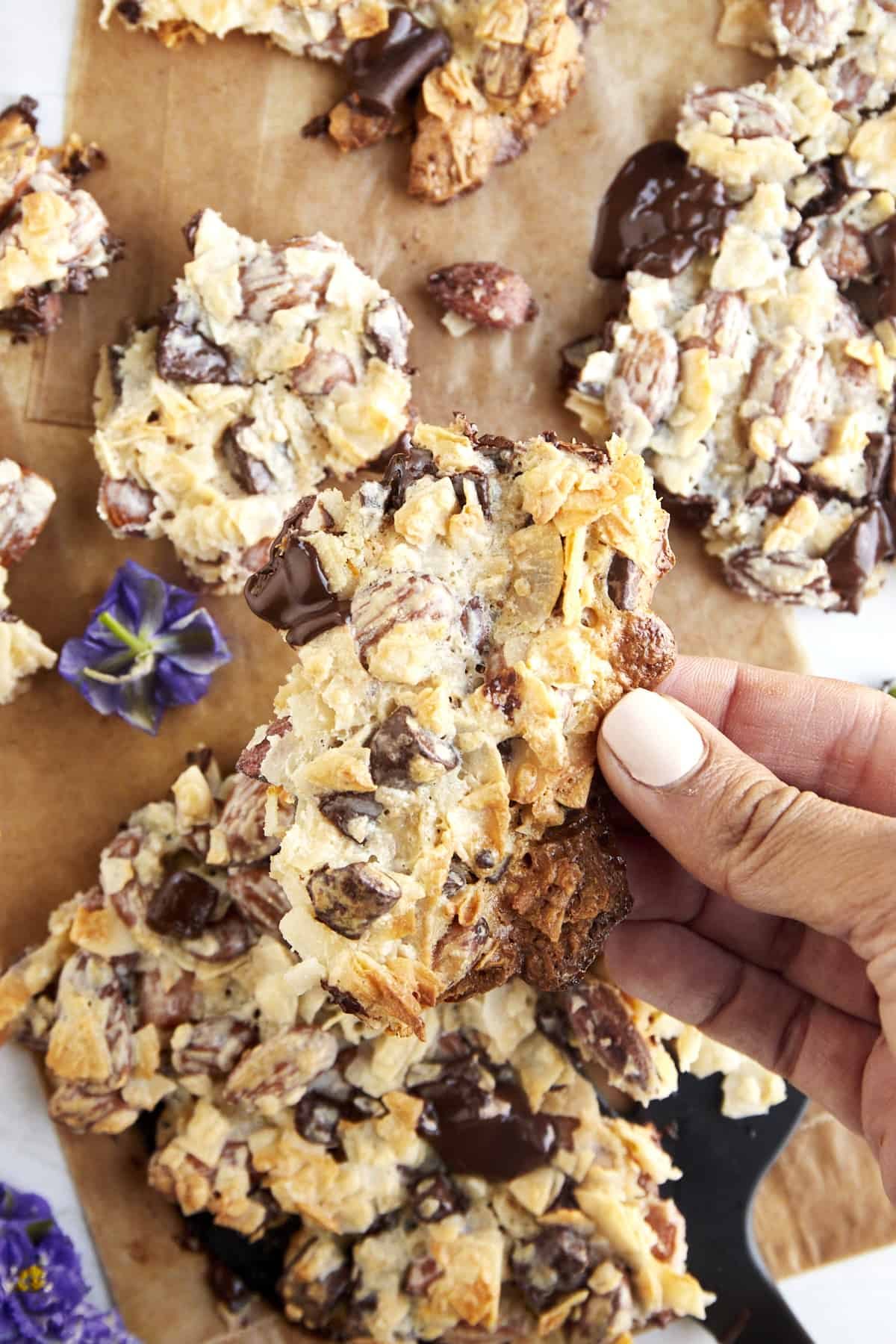 A hand holding a piece of coconut bark with dark chocolate and almonds.