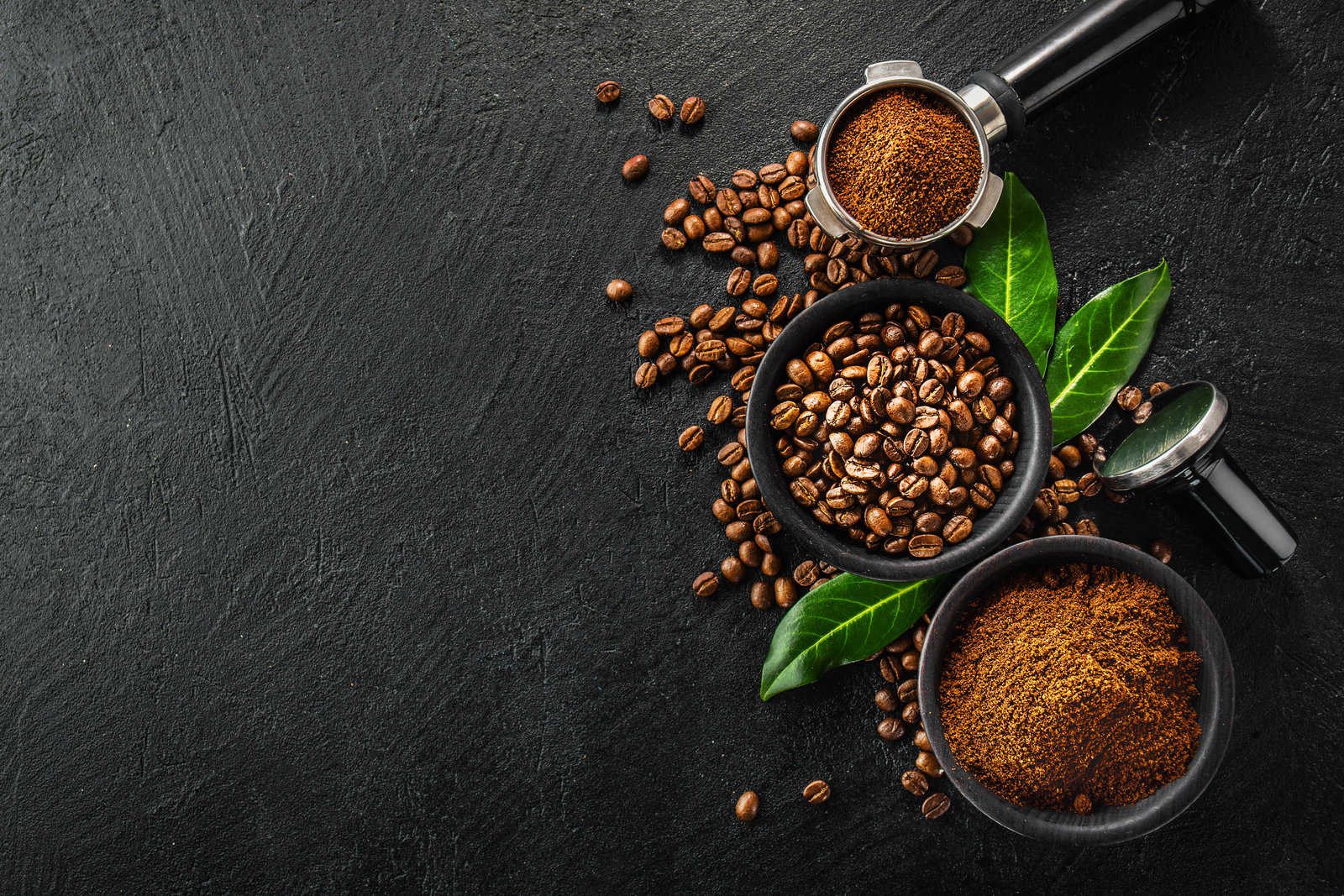 coffee beans and ground coffee in bowls on black background.