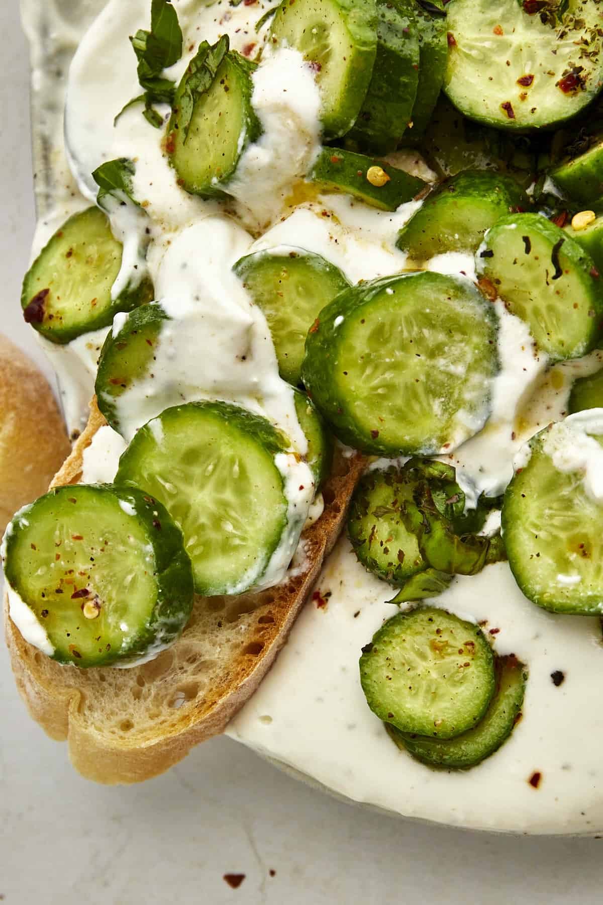 A piece of bread topped with cucumber cottage cheese dip on the edge of a platter of the dip.