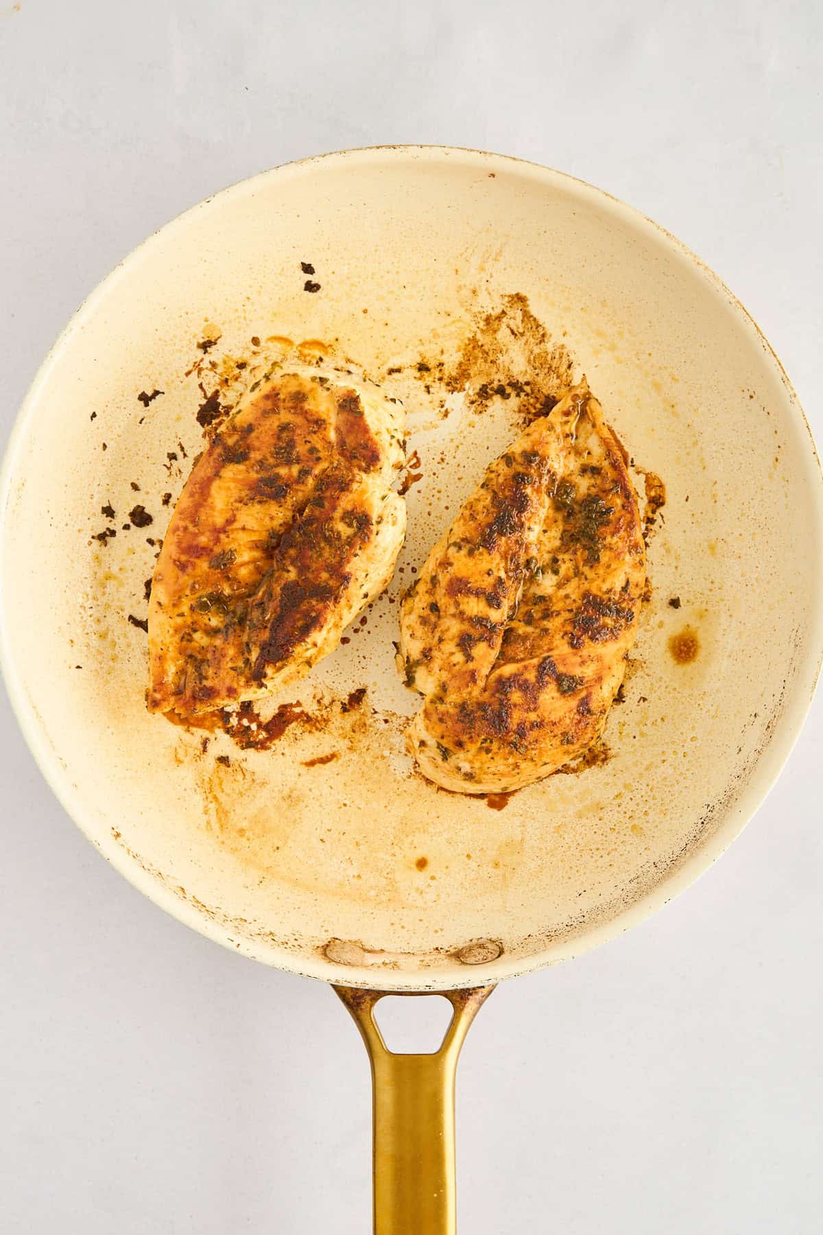 Two chicken breasts cooking in a skillet.