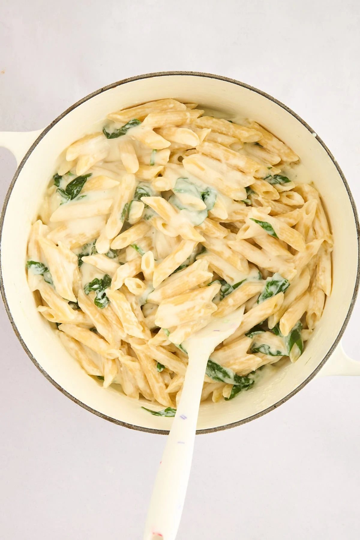 Cottage cheese pasta being tossed with spinach in a pot.