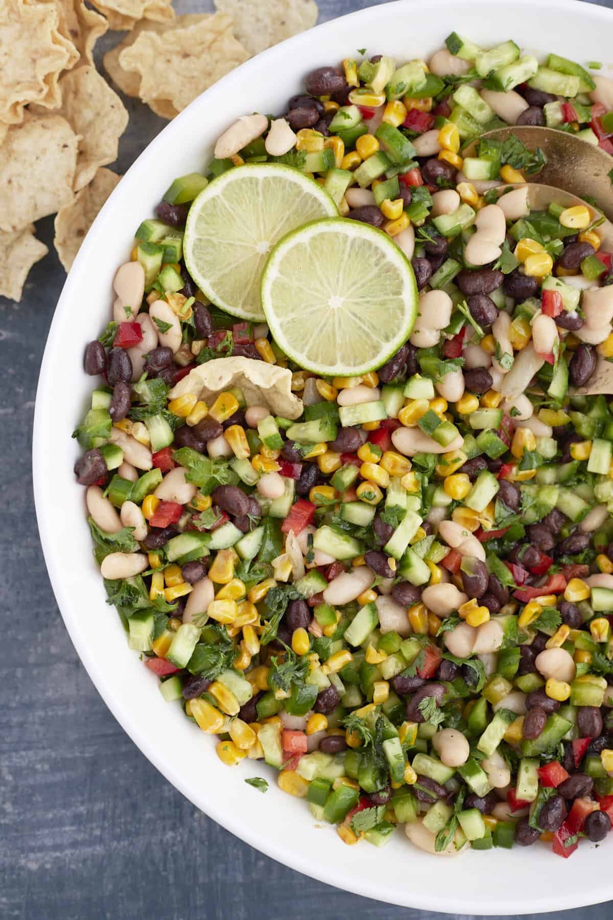 large white bowl with serving spoons, cowboy caviar and garnish with limes