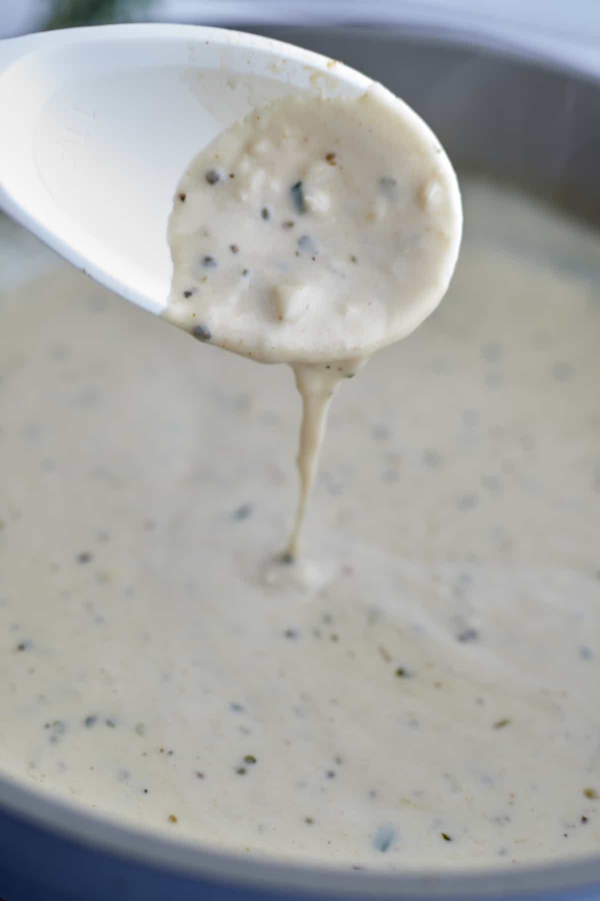 a white spoon ladling creamy white sauce out of a skillet.