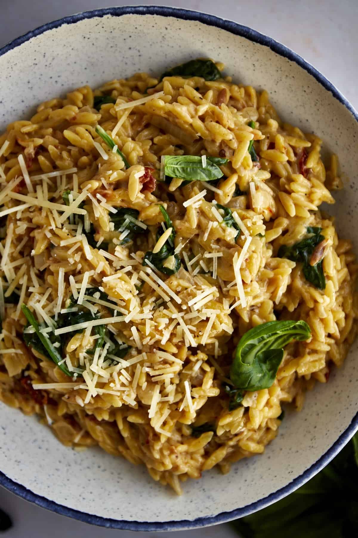 A bowl of of creamy one pot Tuscan orzo pasta topped with Parmesan and fresh basil.