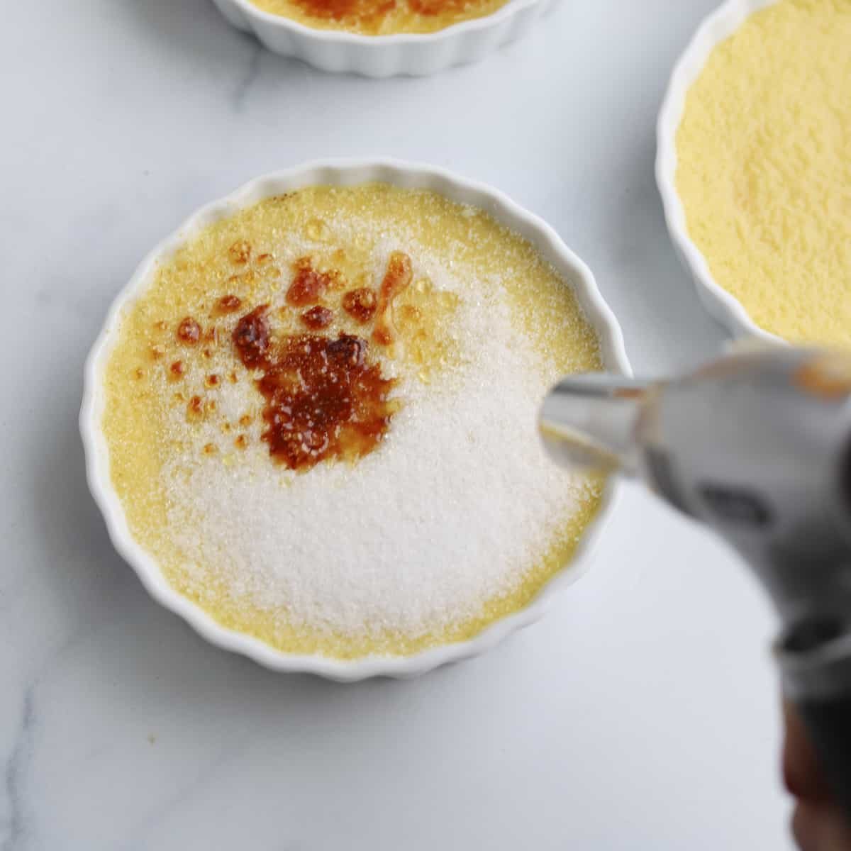 A hand uses a kitchen torch to caramelize sugar.