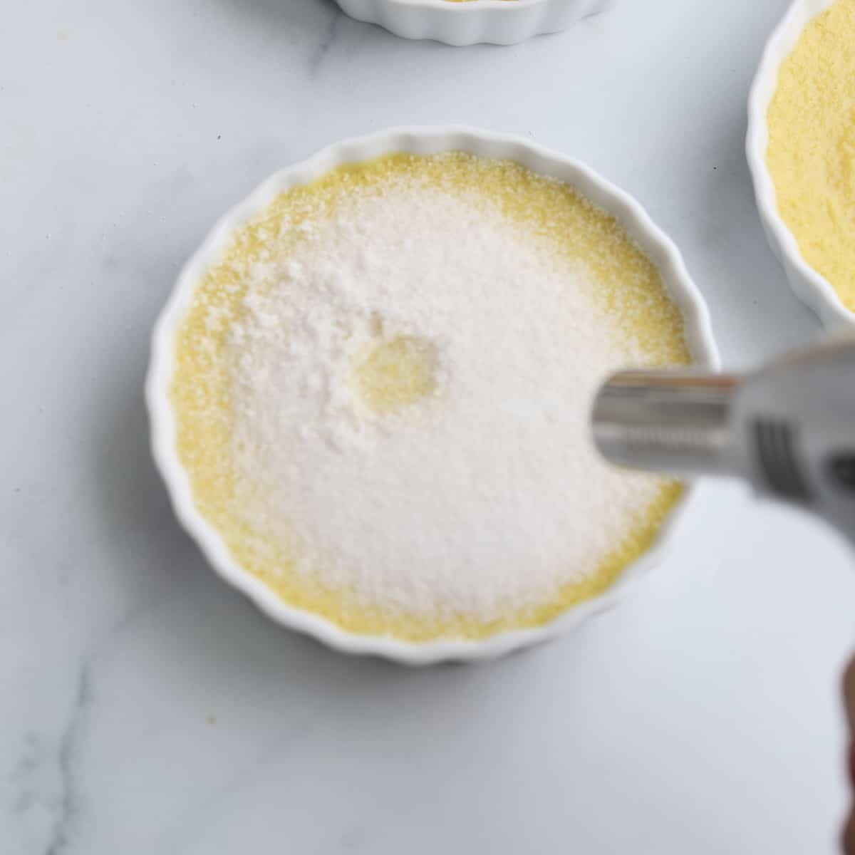 A kitchen torch is being used to caramelize a layer of sugar.