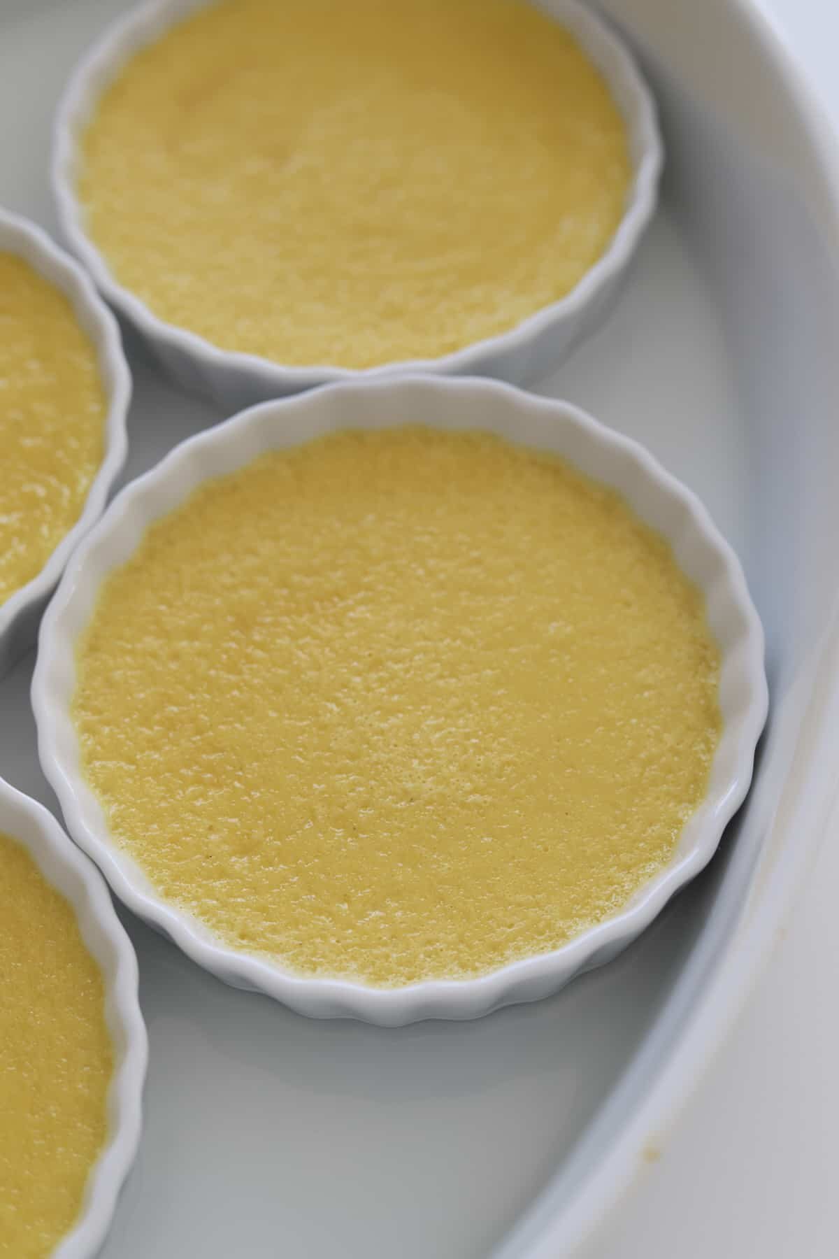 Four round white ramekins filled with smooth, yellow custard.