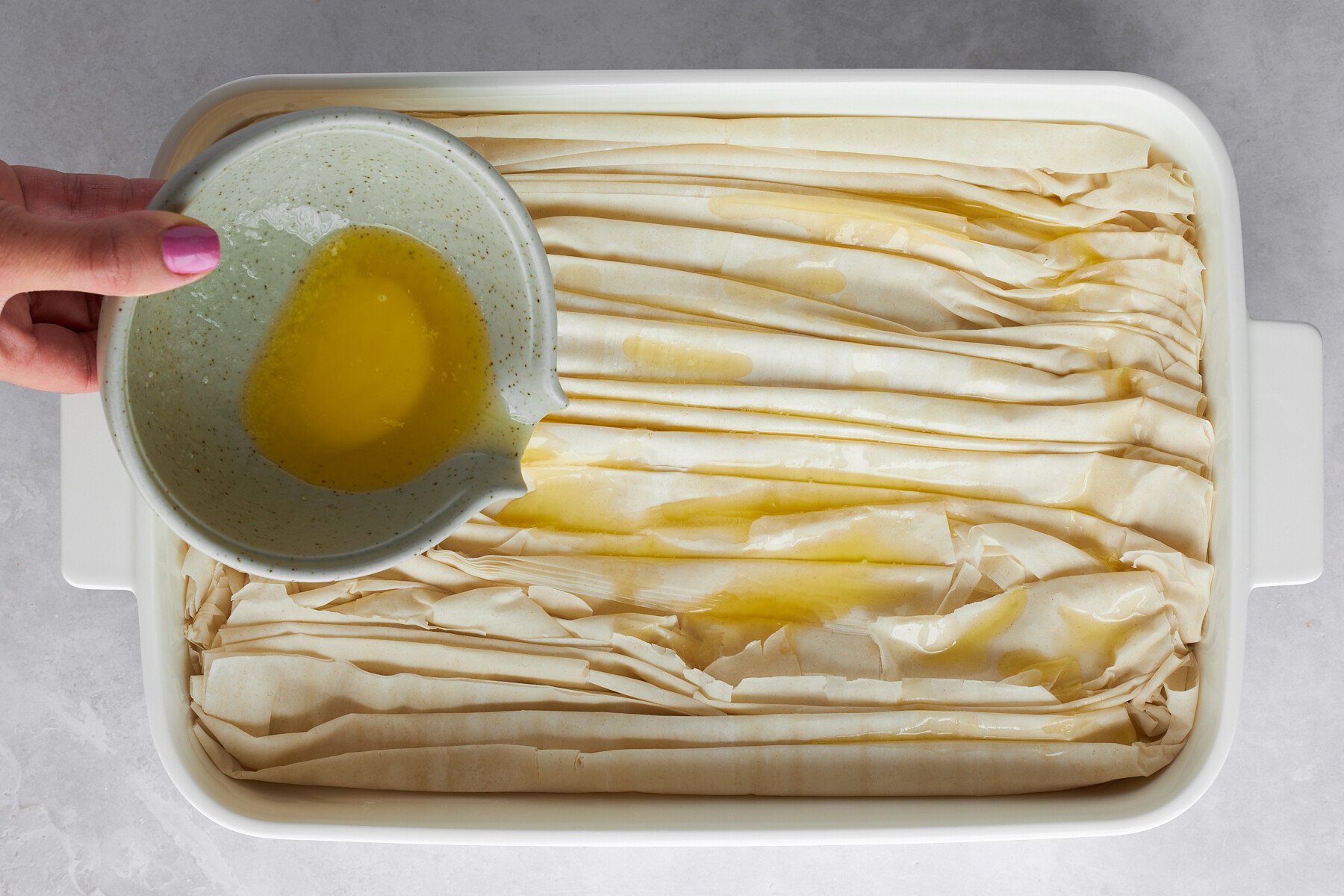 Melted butter being poured over crinkled phyllo dough.