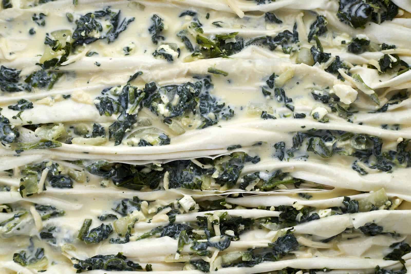 crinkle phyllo dough stuffed with spanakopita filing in a baking dish topped with a milk and yogurt mixture.