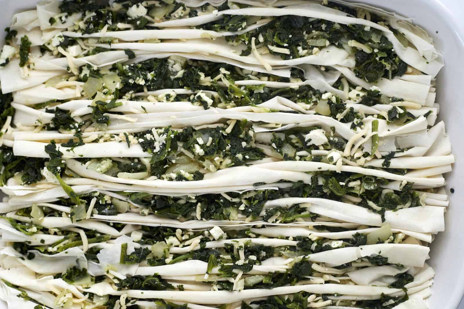 crinkle phyllo dough stuffed with spanakopita filing in a baking dish.