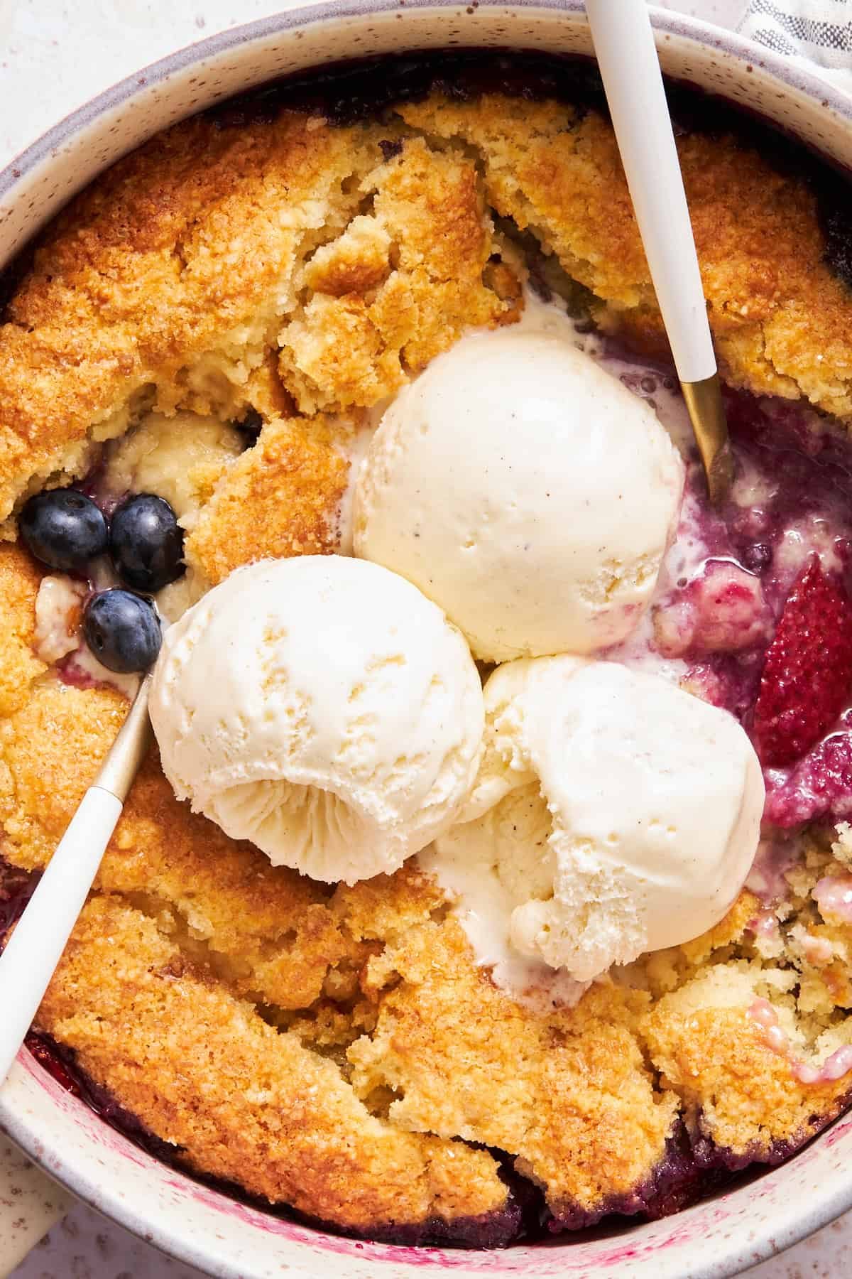 Close up view of mixed berry cobbler topped with three scoops of vanilla ice cream.