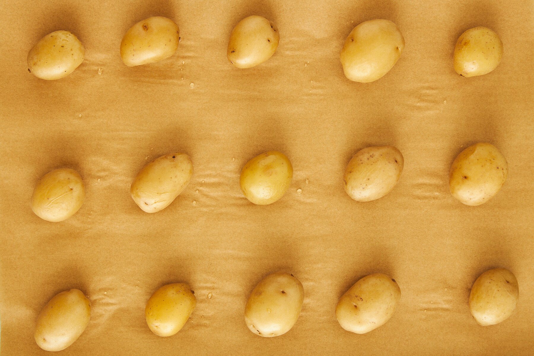 Boiled potatoes on a parchment paper-lined baking sheet.