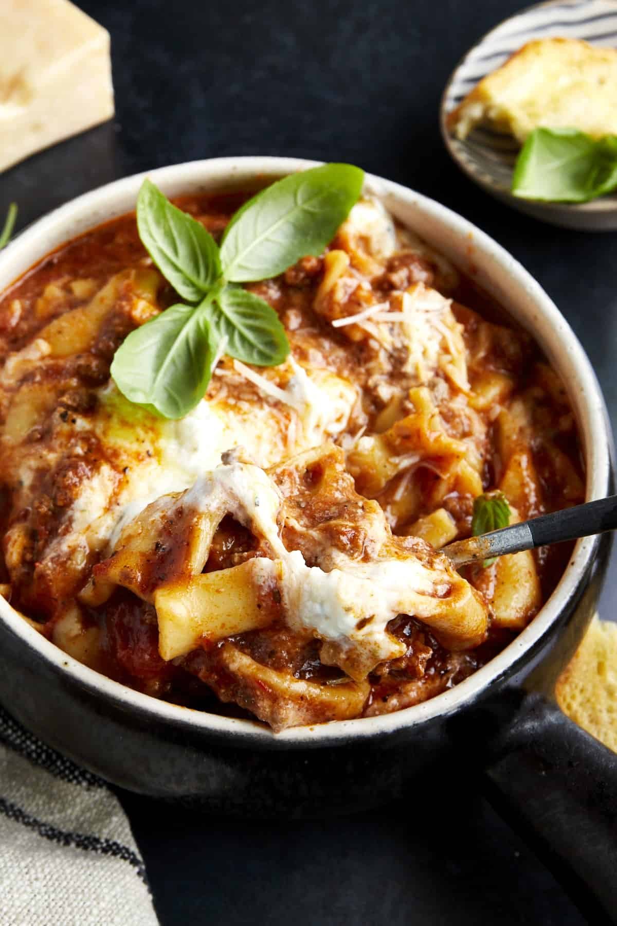 A spoon sticking out of a bowl of crockpot lasagna soup with fresh basil on top.
