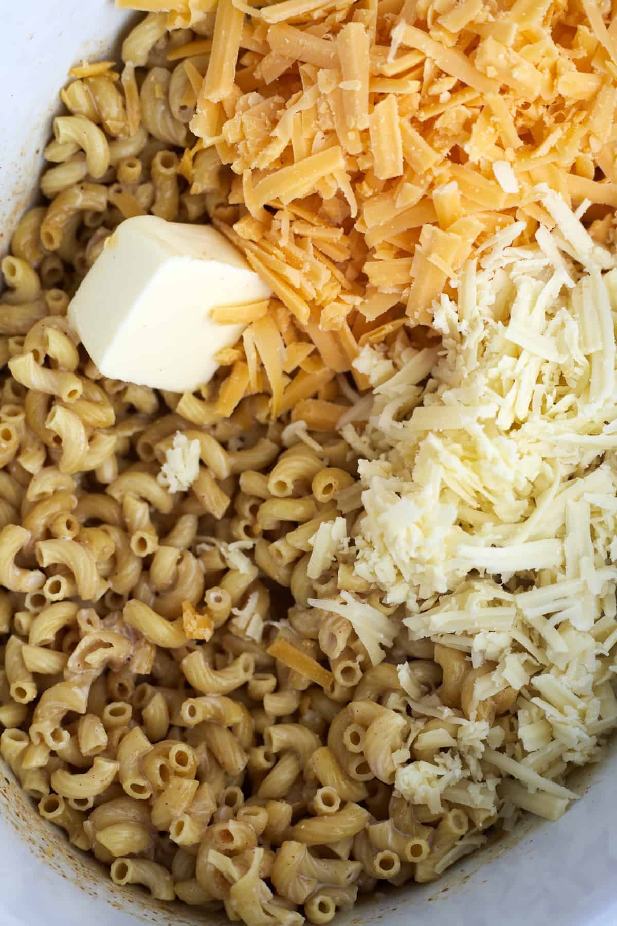 cooked elbow noodles, white and yellow cheddar cheese, and butter in a crockpot.