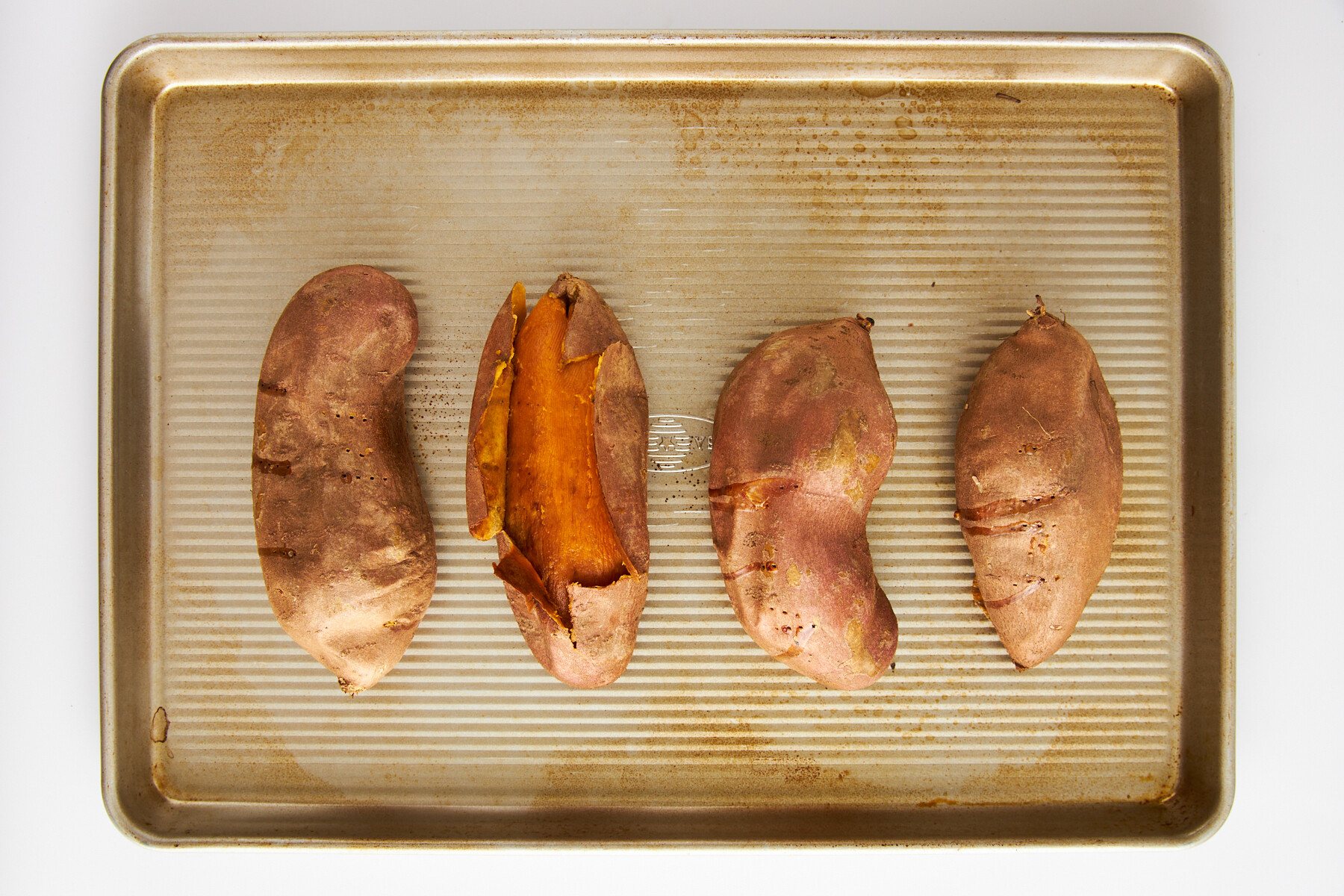 Four roasted sweet potatoes on a baking sheet.