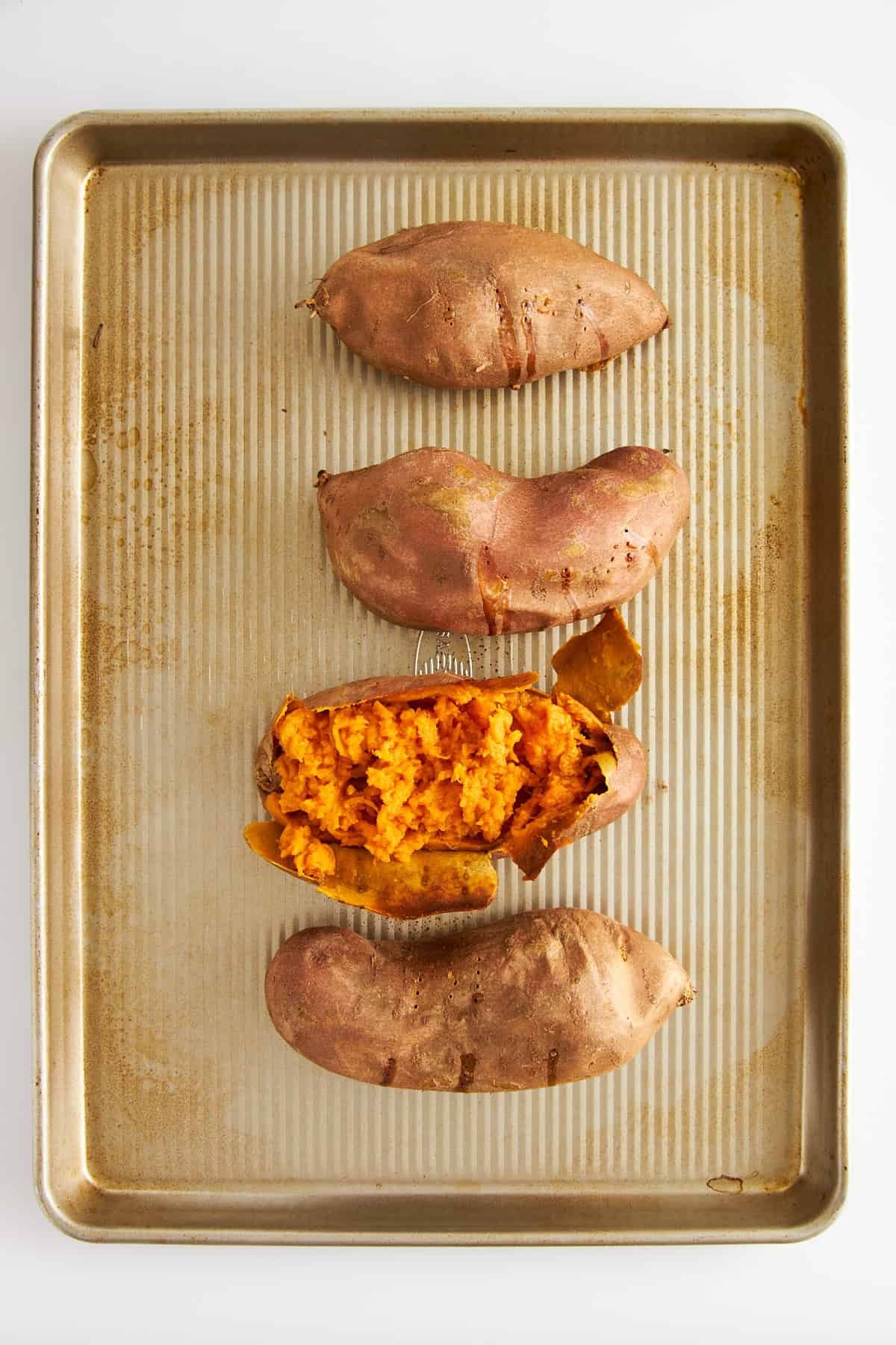 Four baked sweet potatoes with one exposed to show the soft center.