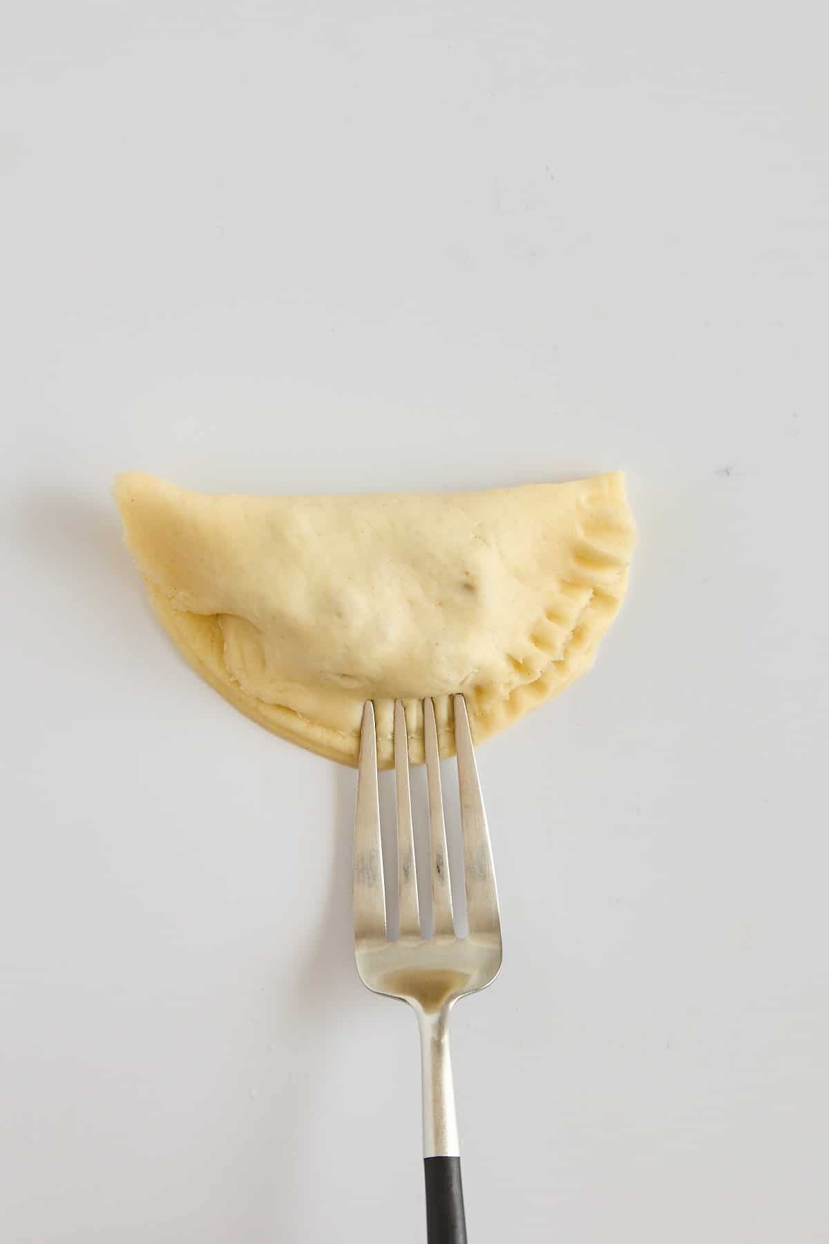A fork crimping the edges of a pecan hand pie.