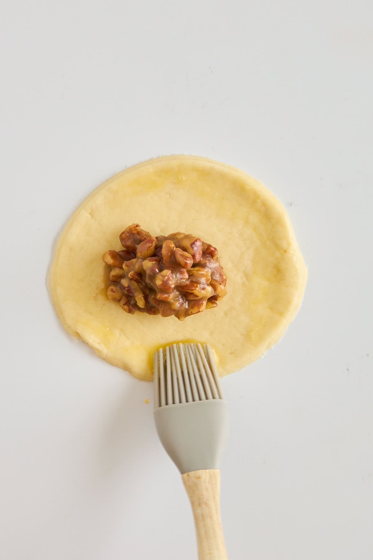 A circle of pie dough with pecan pie filling being brushed with egg wash.
