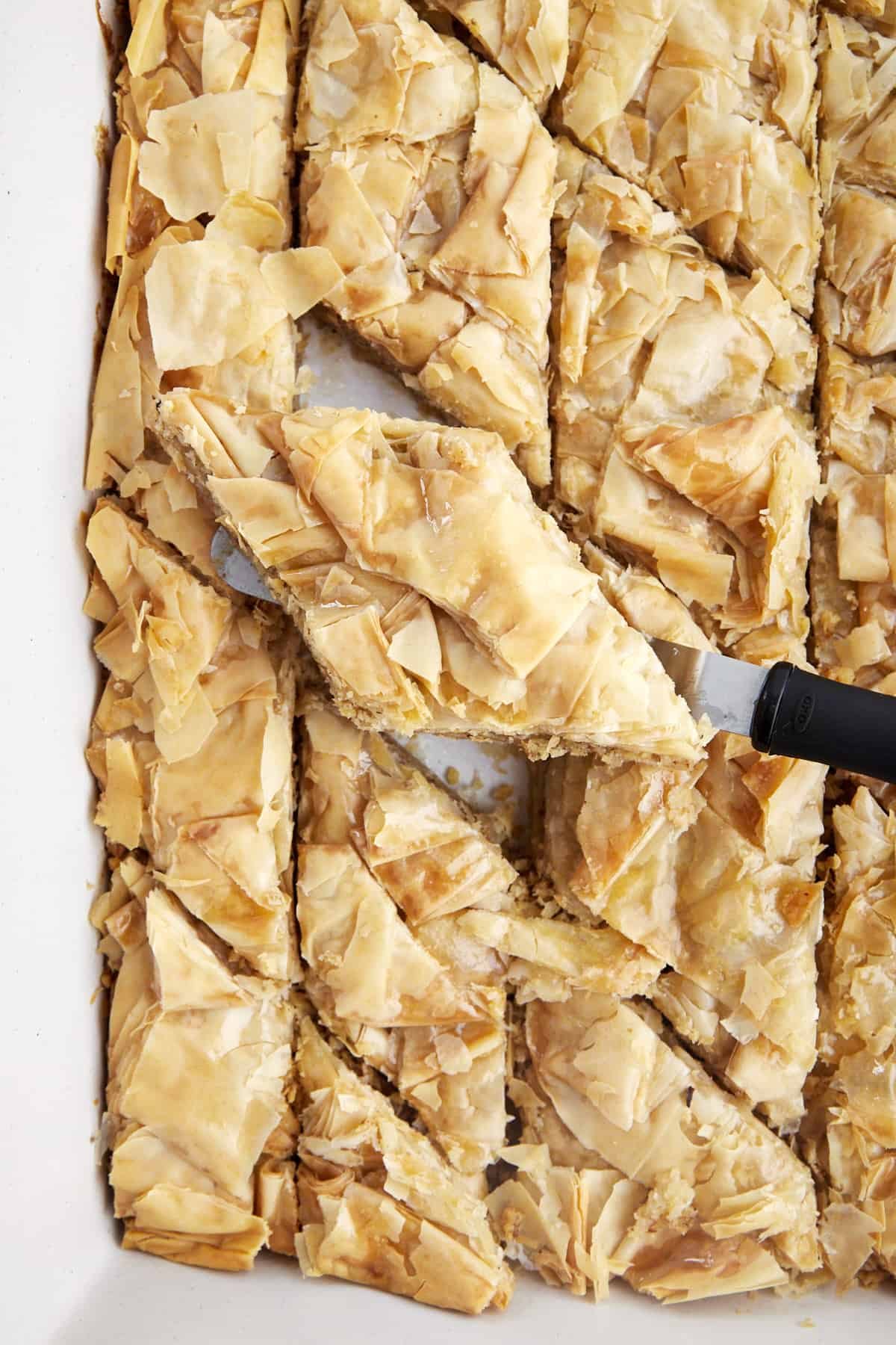 a piece of baklava being lifted from a full baking dish.