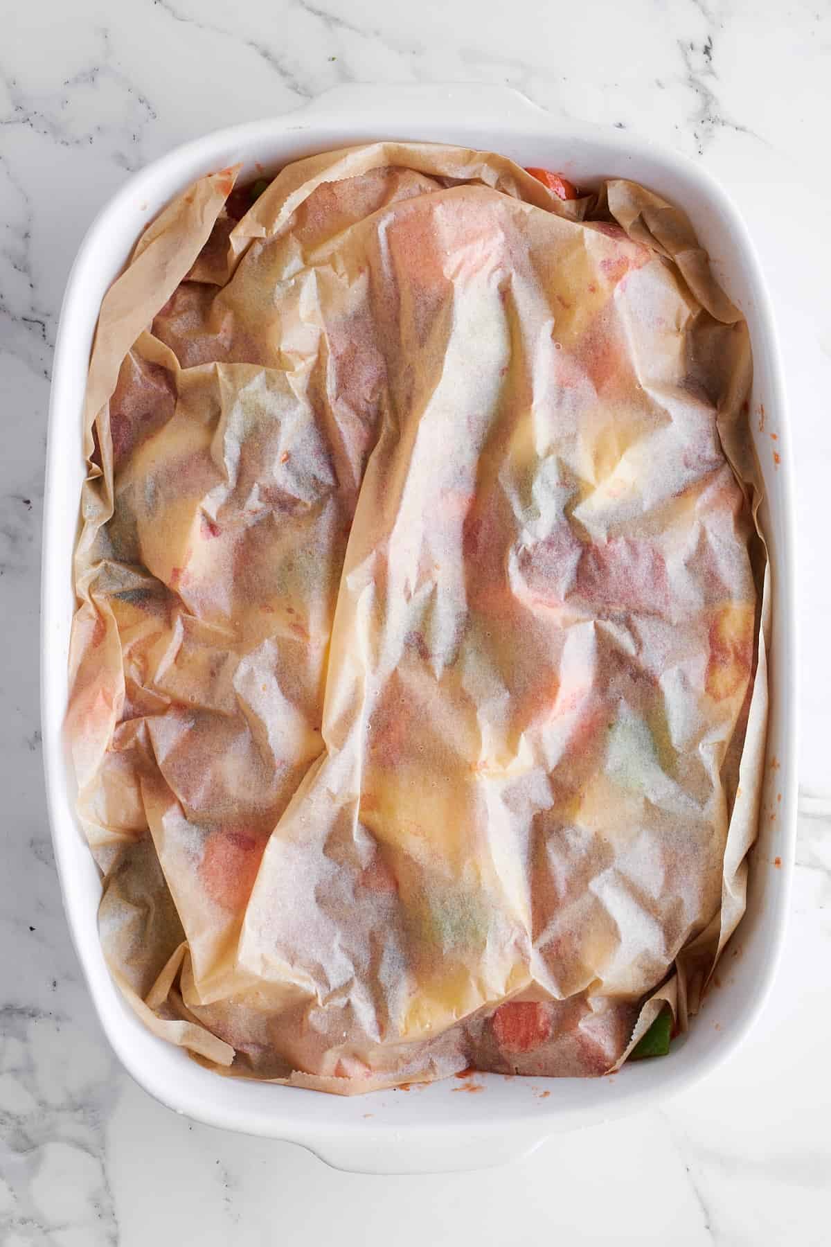 A casserole dish full of beef and veggies topped with parchment paper.