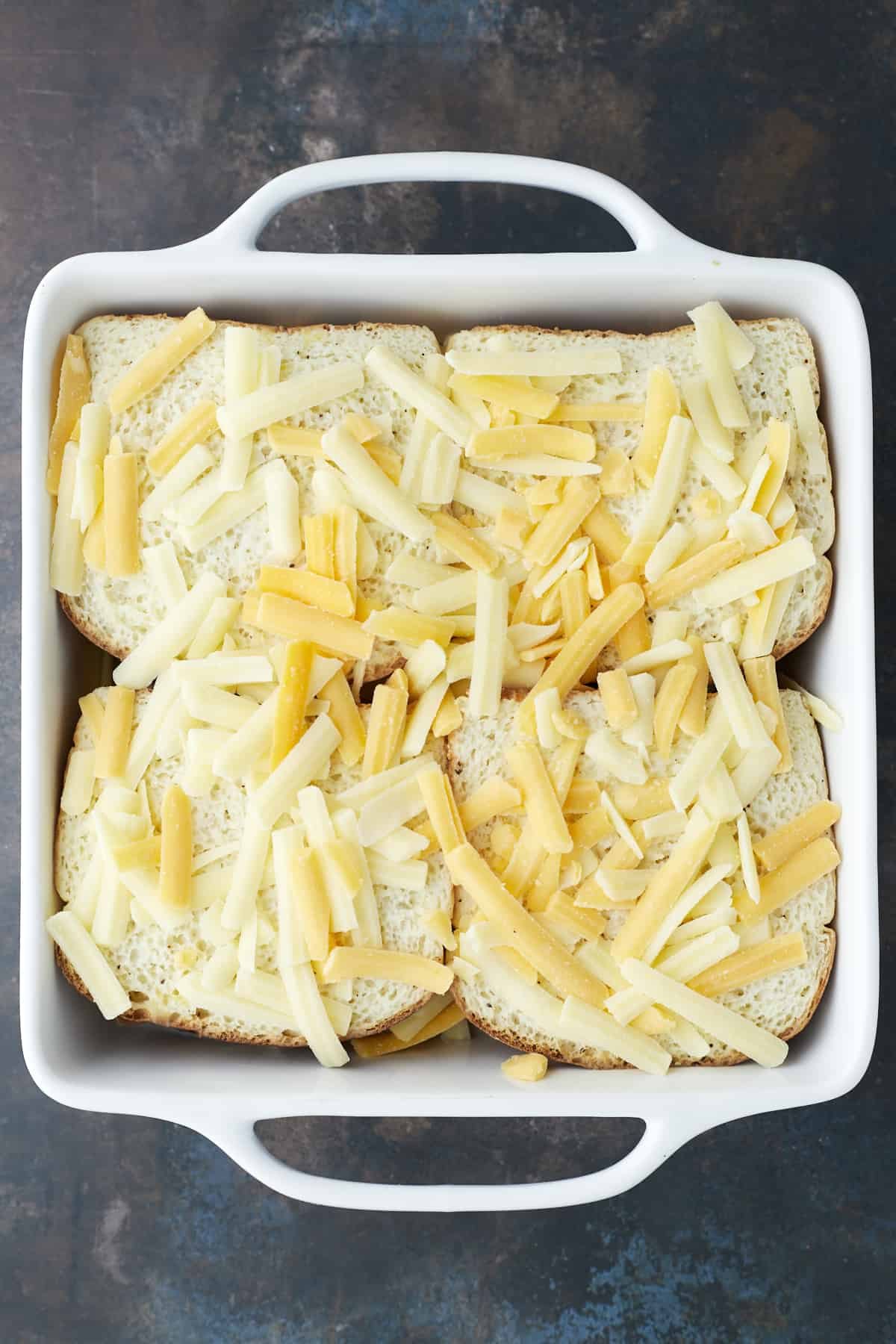 four unbaked fajita chicken sandwiches topped with shredded cheese in a white square baking dish