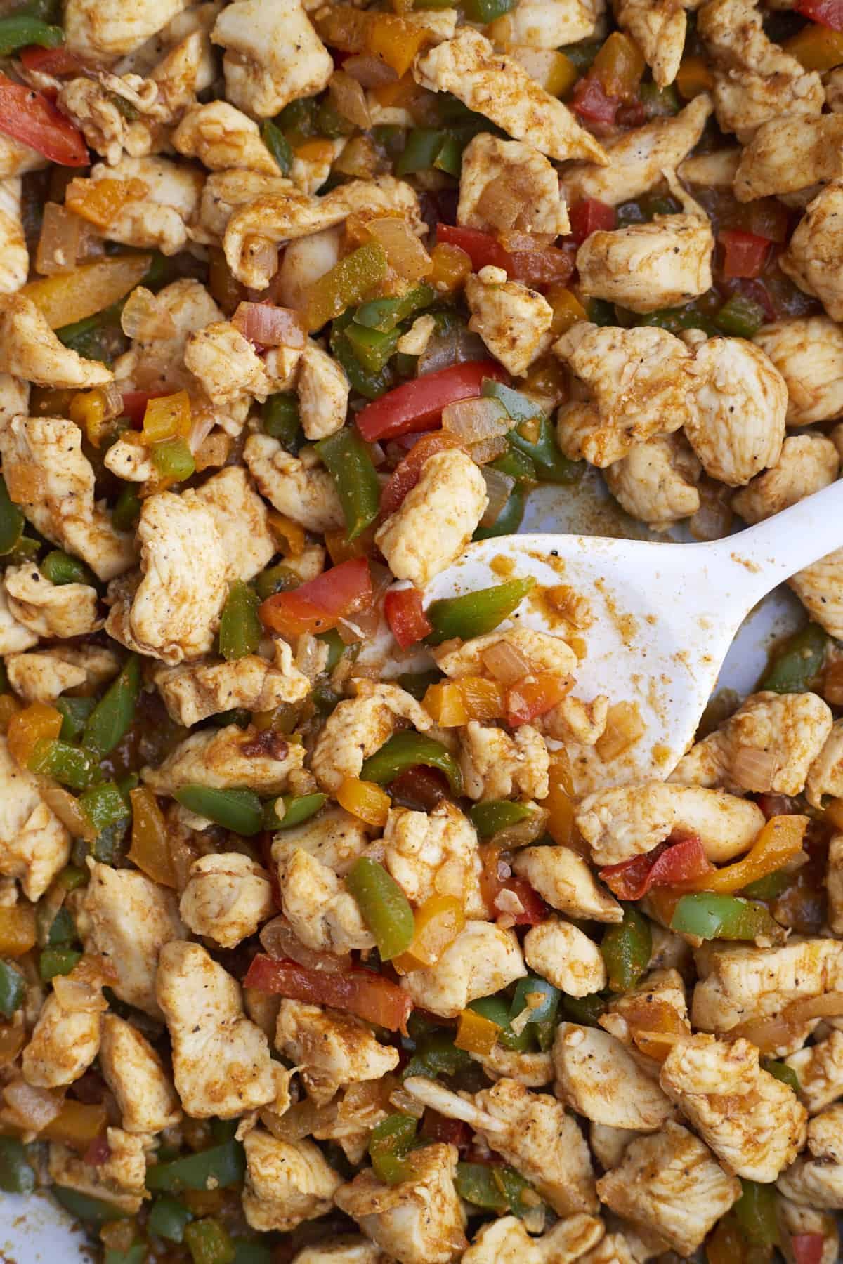 chicken fajita mixture with peppers and onions being stirred with a spoon