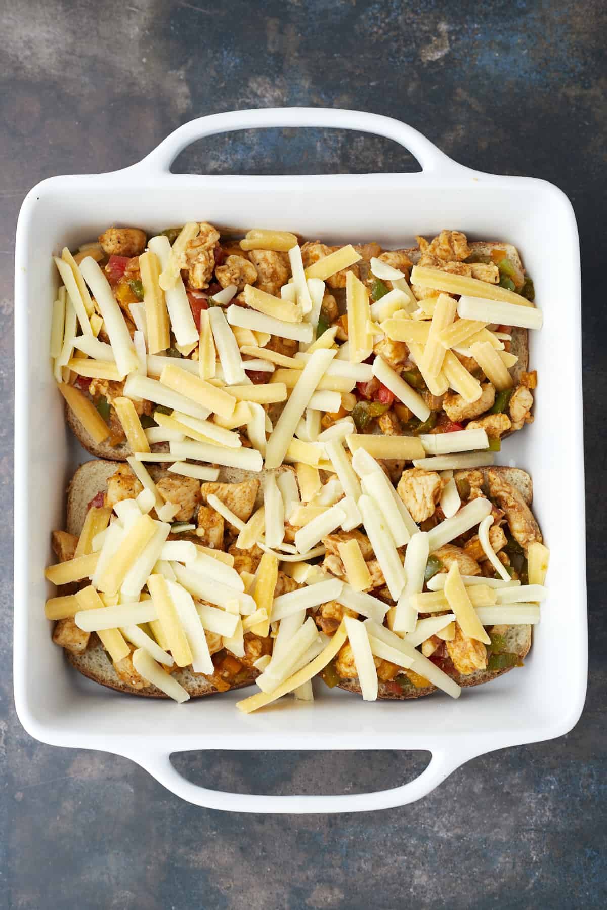 four pieces of bread in a baking dish topped with fajita chicken and cheese