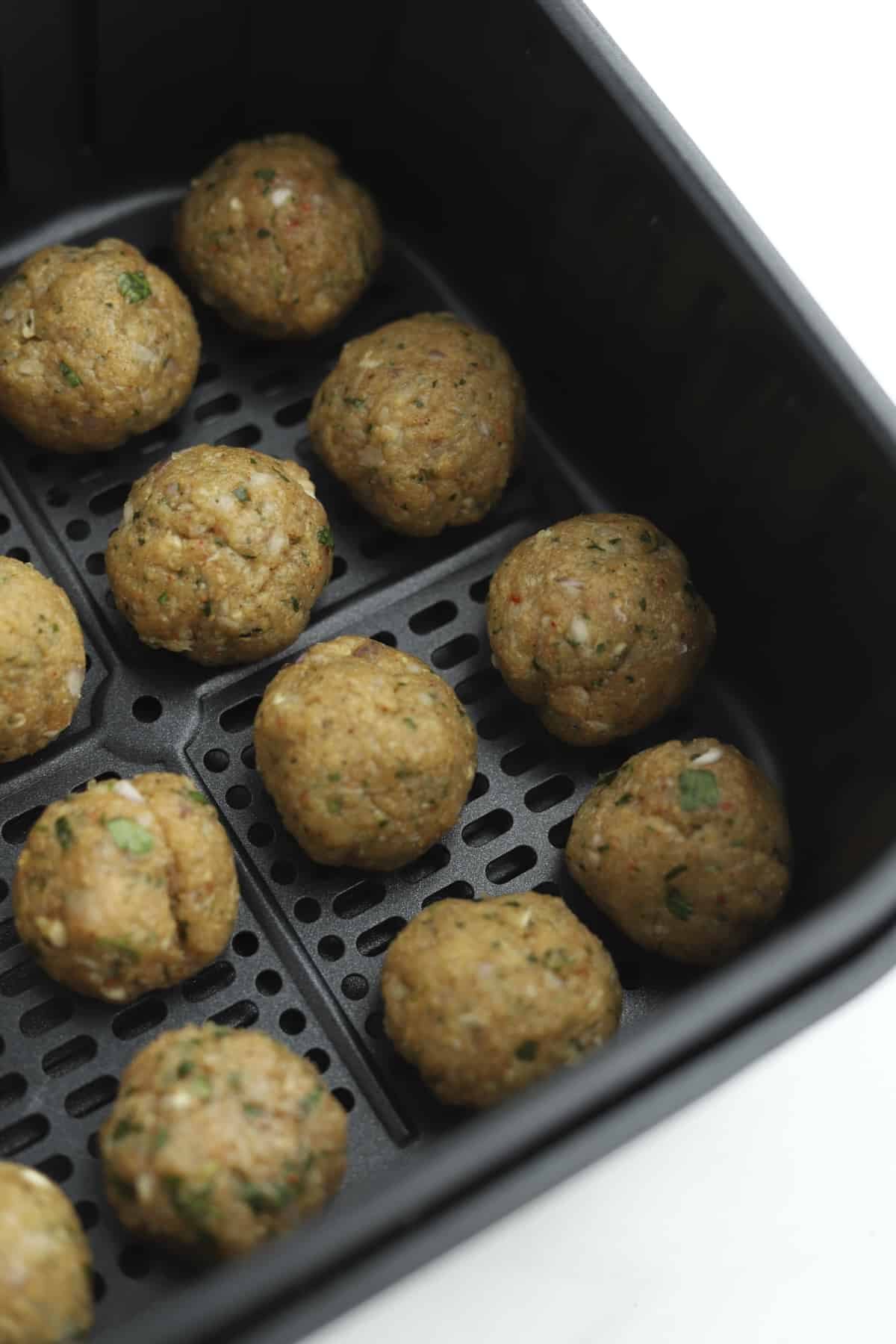 Raw chicken kofta meatballs in an air fryer basket.