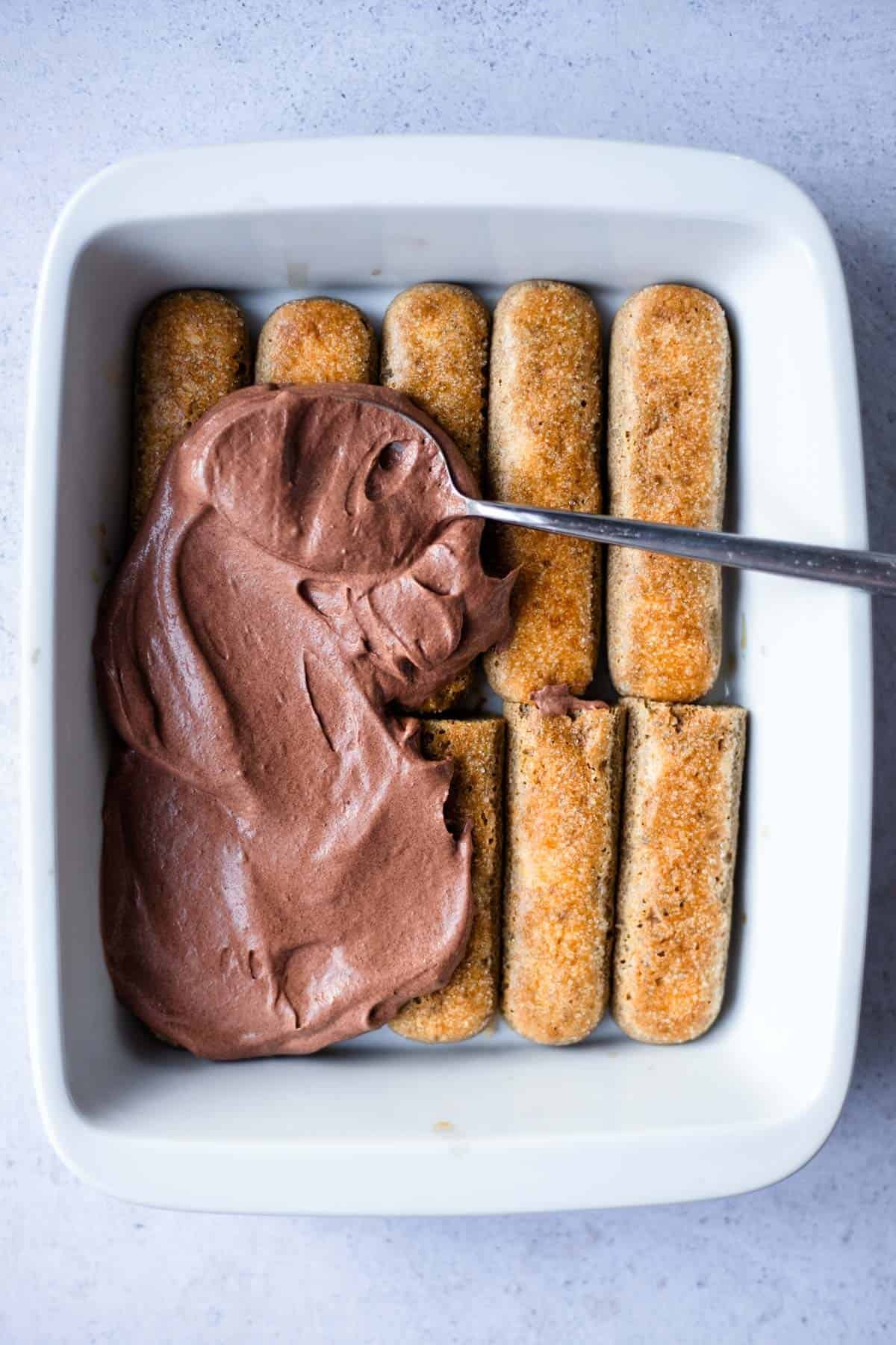 chocolate mascarpone being spread over a layer of ladyfingers.