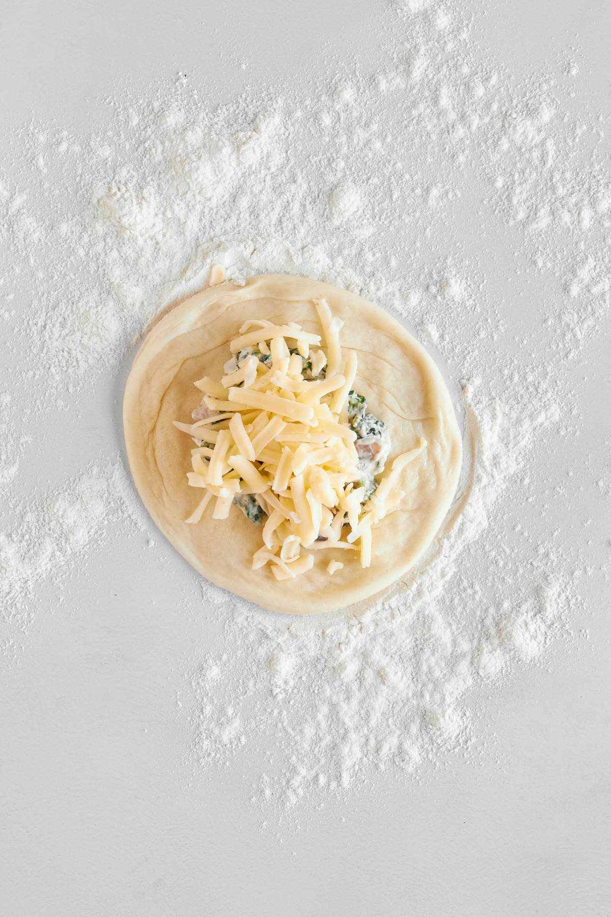 A flattened dinner roll topped with a spinach and cheese filling and shredded cheese.