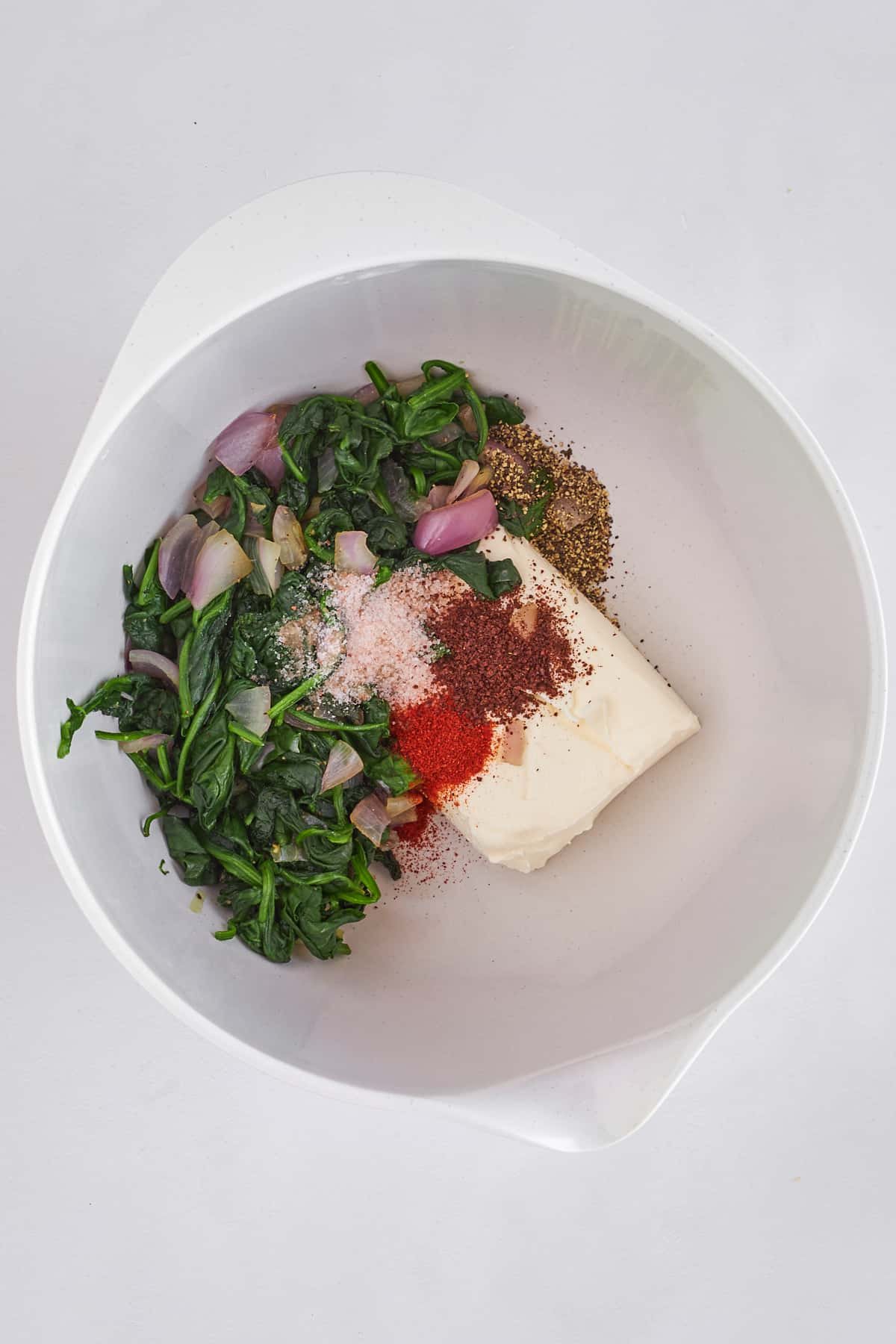 Sautéed spinach, shallot, spices, and cream cheese in a bowl.