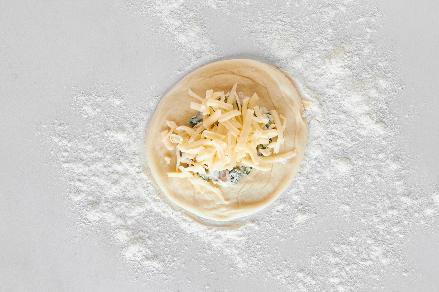 A dinner roll topped with a spinach and cheese mixture and shredded cheese.