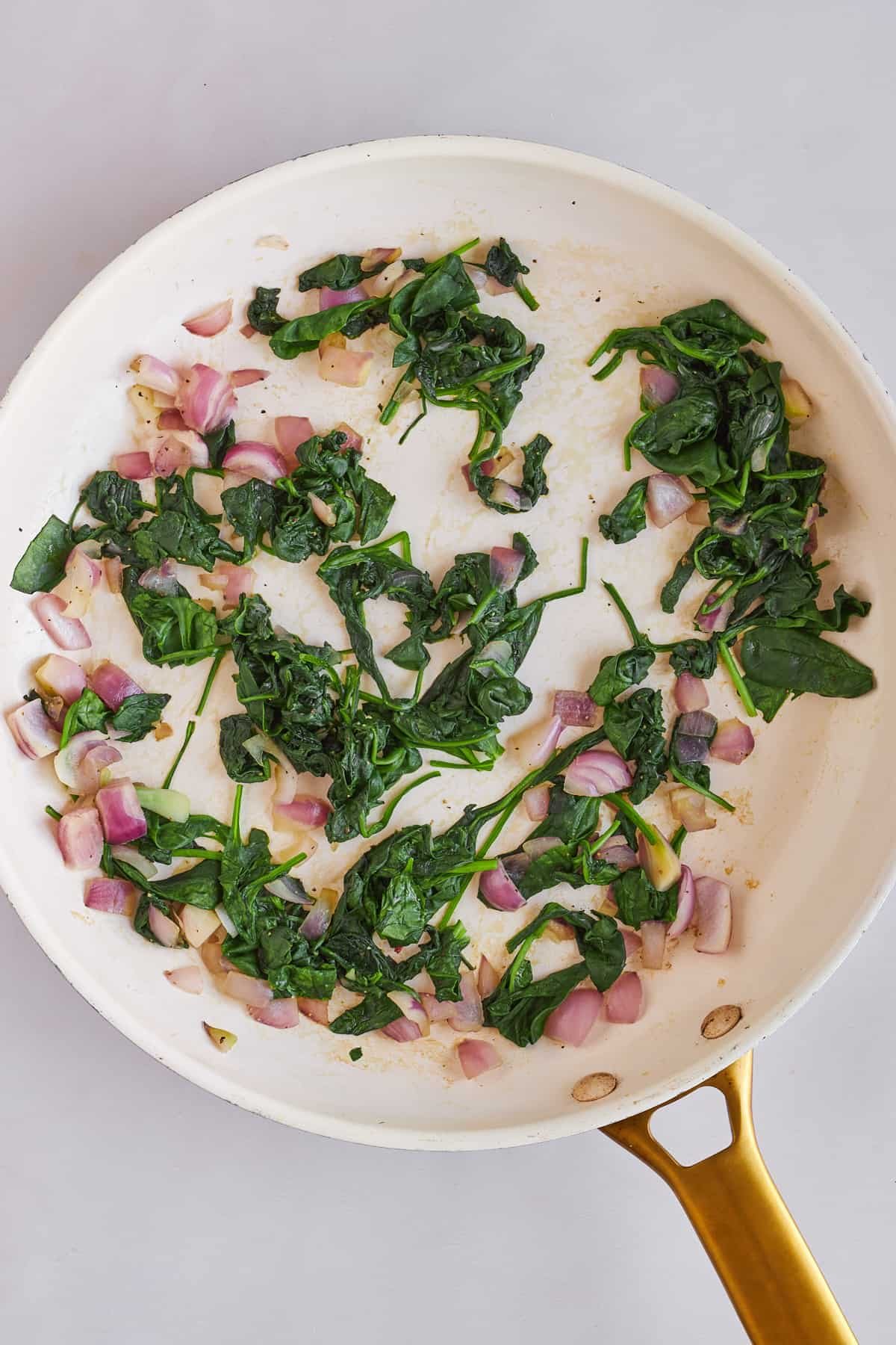 Sautéed spinach and shallot in a skillet.