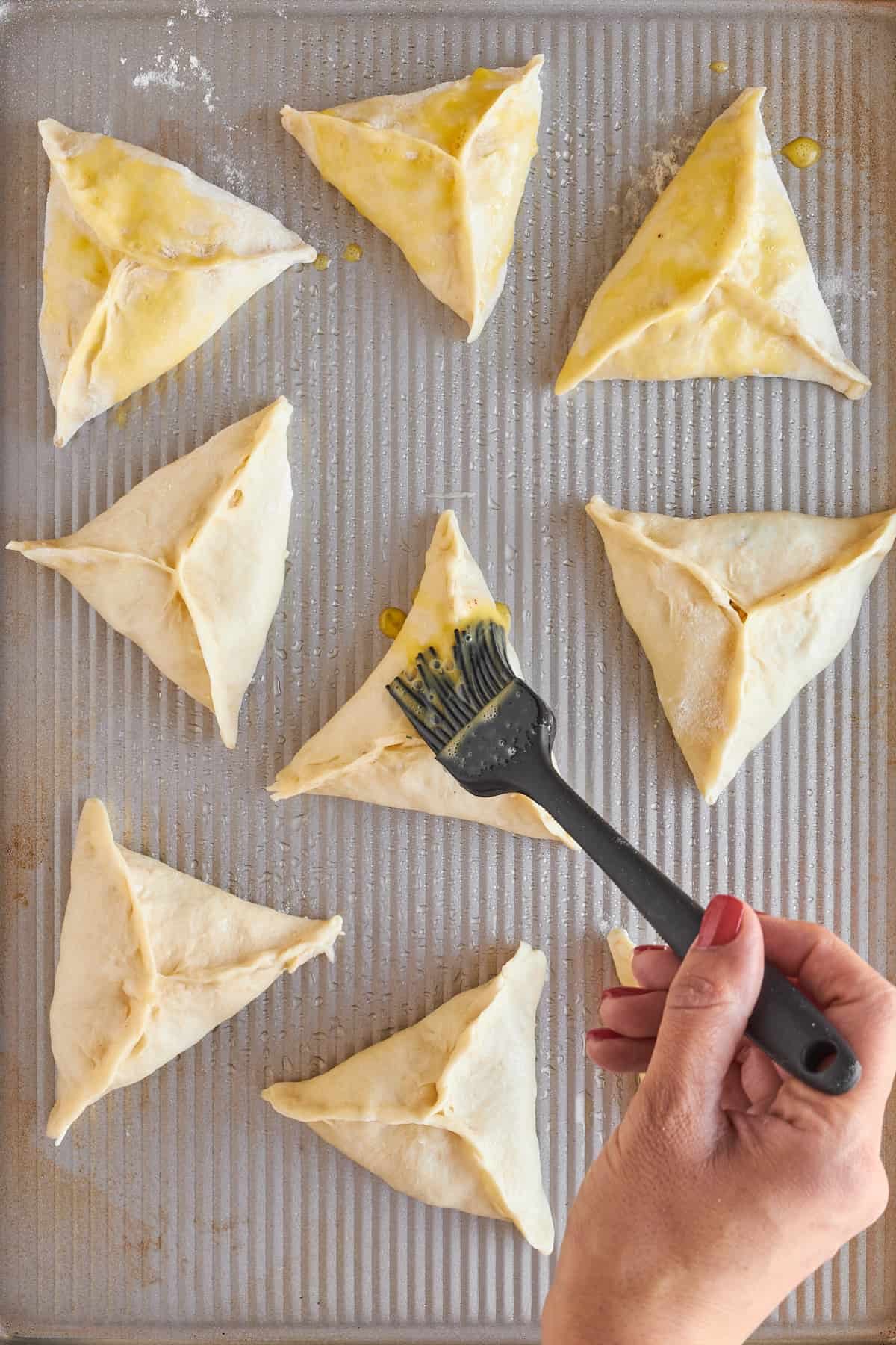 Raw fatayer on a baking sheet being brushed with olive oil.