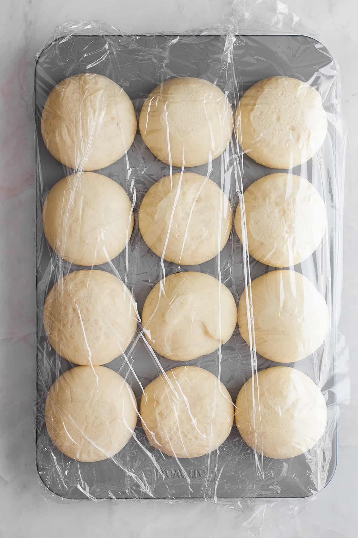 Risen bread rolls in a muffin tin.