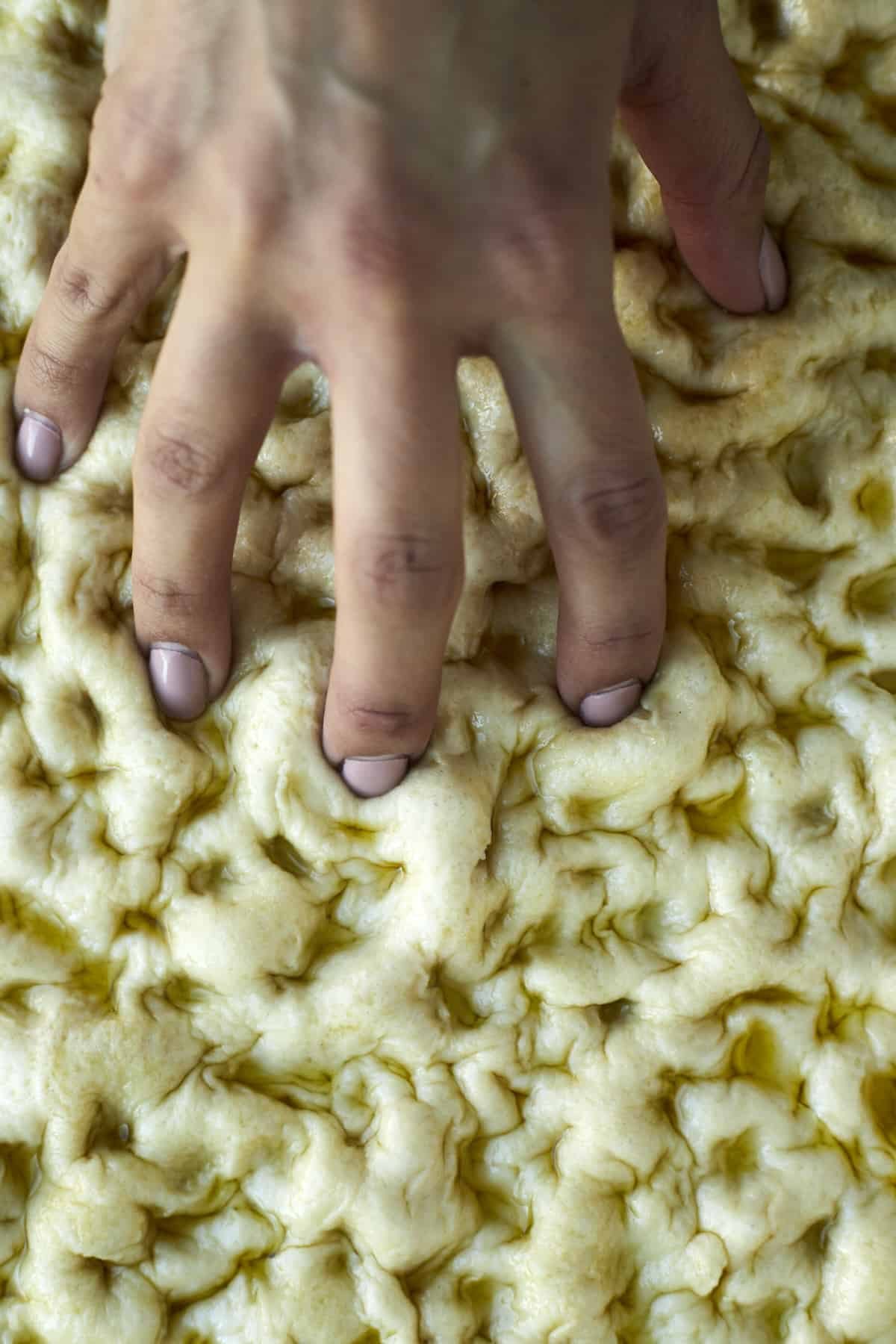 a hand making indentations into raw bread roll dough
