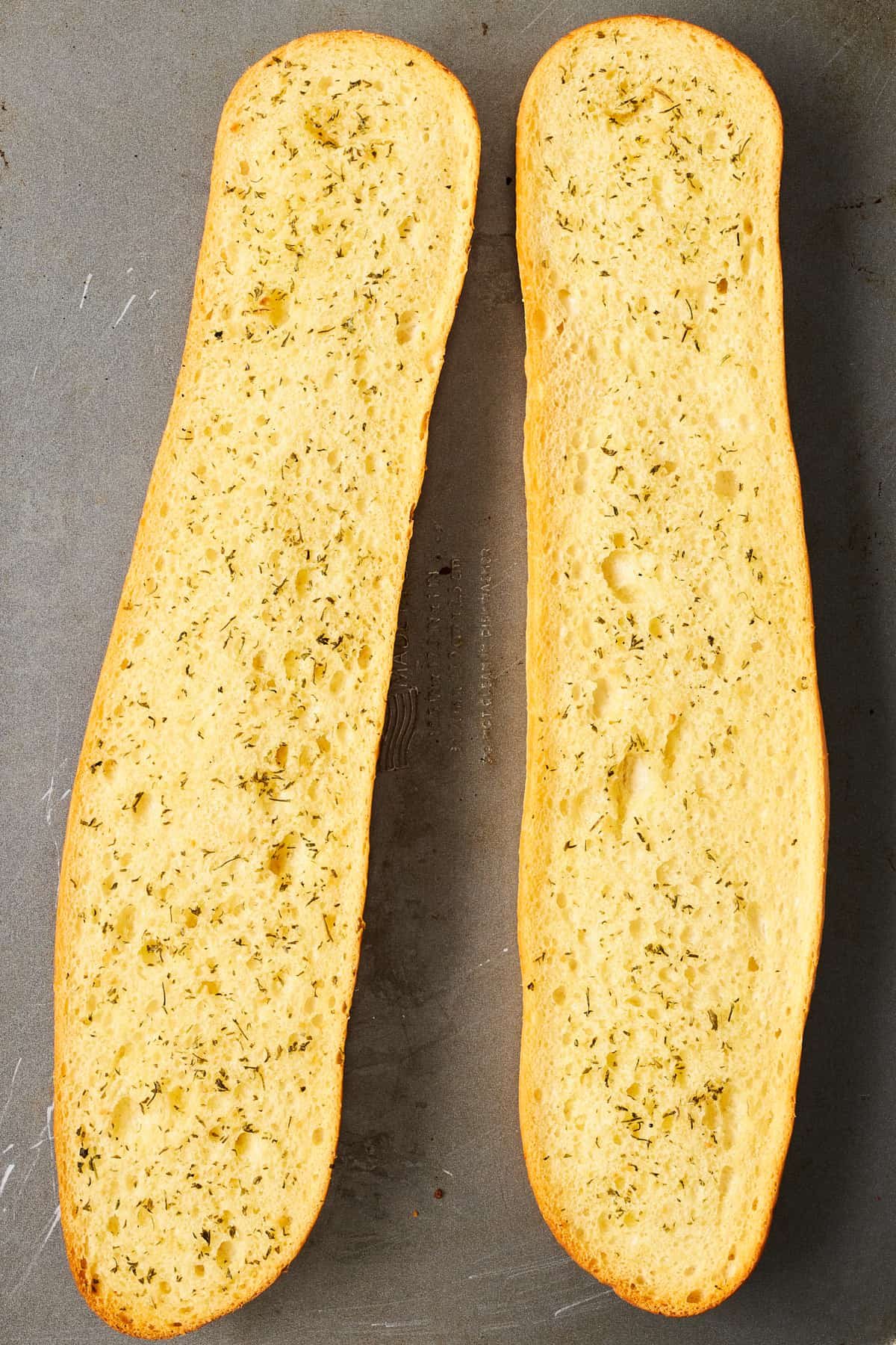 Two halves of a baguette topped with herbed butter.