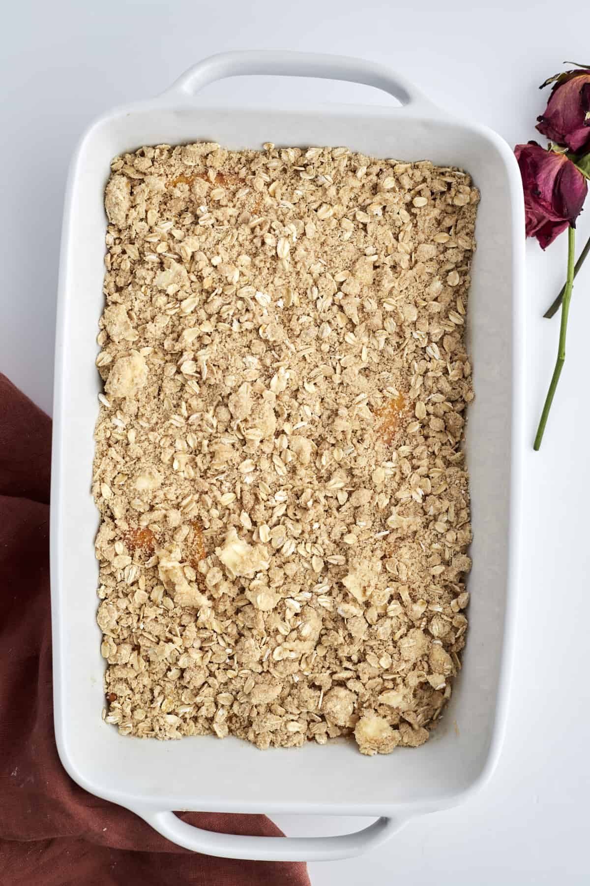 overhead image of an unbaked peach crisp in a white baking dish.