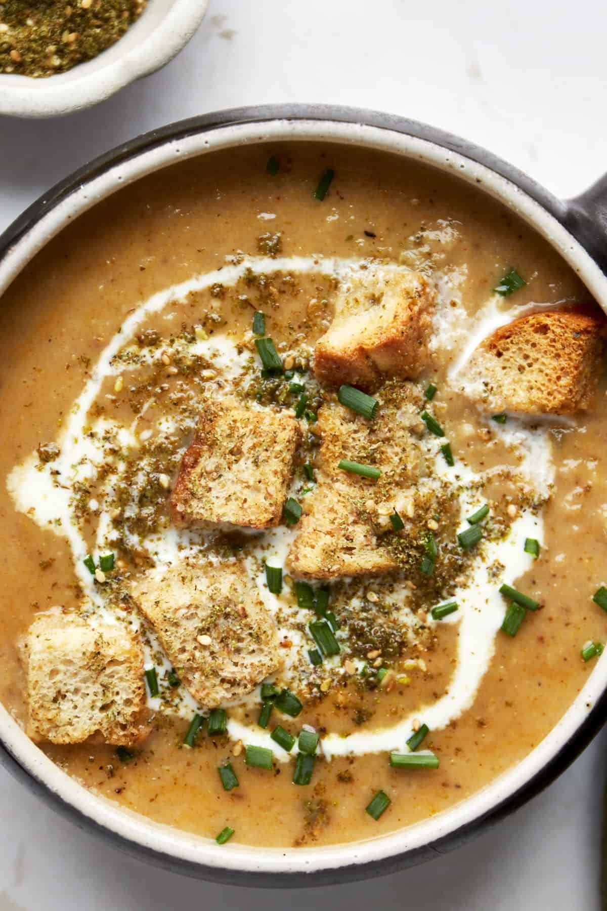 A bowl of roasted cauliflower soup topped with heavy cream, croutons, and za'atar.